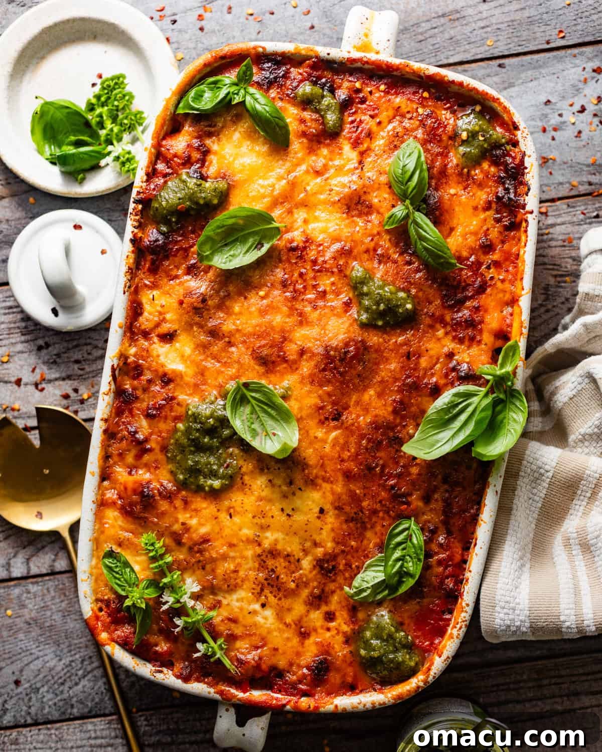Baked ziti in a baking pan with fresh basil and pesto garnishes on top, showcasing a golden, bubbly crust.