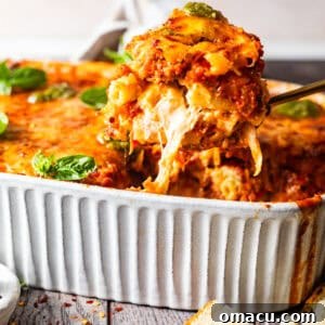 A spoon pulling up baked ziti out of a baking dish to see the cheese pull, showcasing the layers.