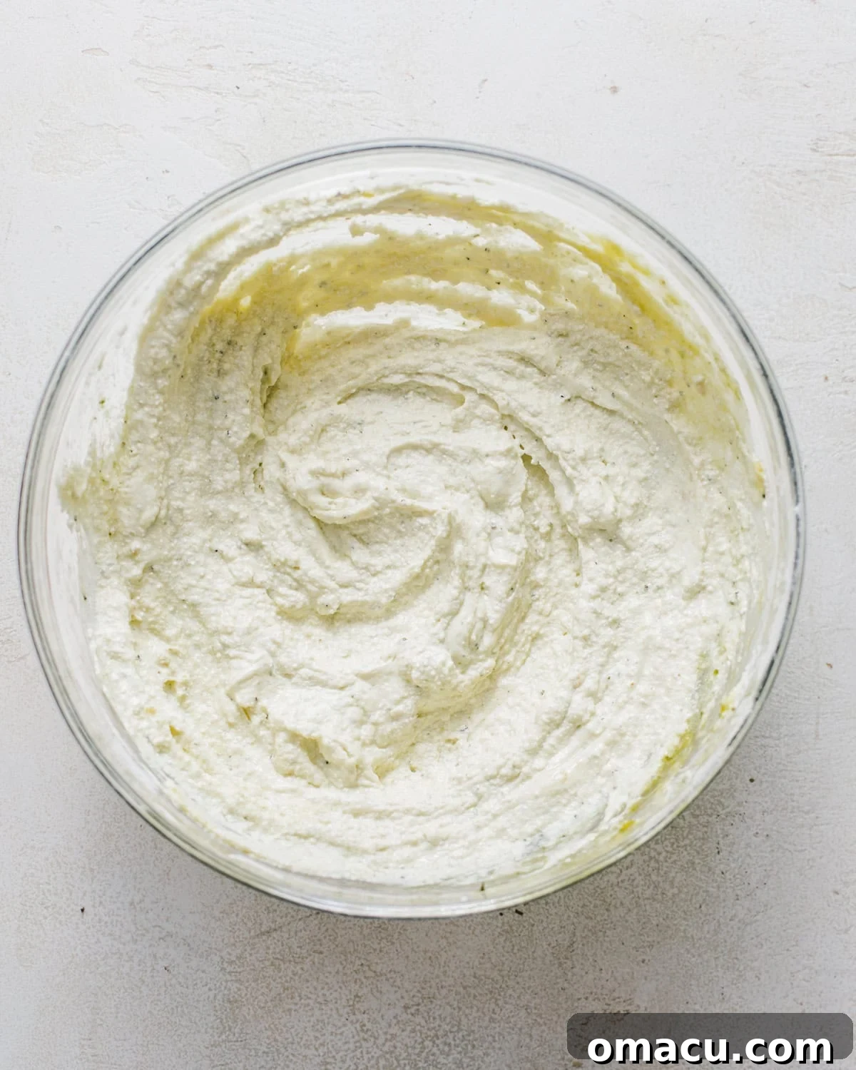 Creamy ricotta mixture blended with vibrant green pesto in a mixing bowl.