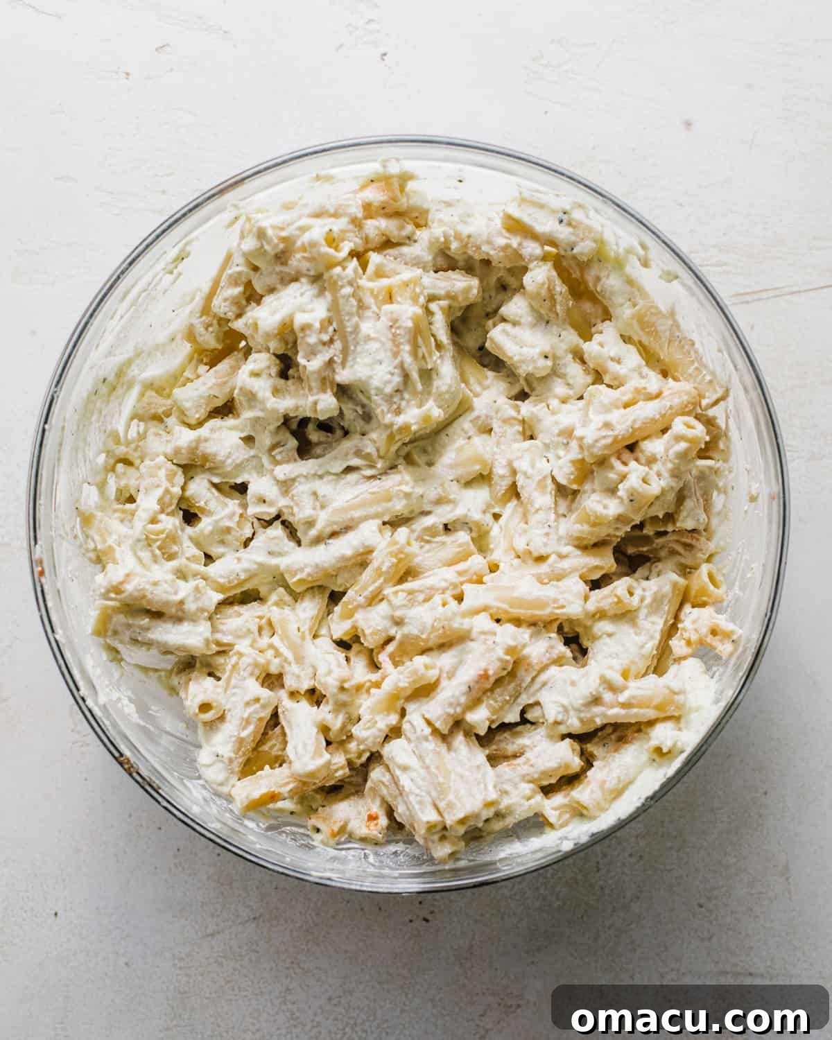 Cooked ziti pasta being tossed with the creamy ricotta and pesto mixture in a large bowl.