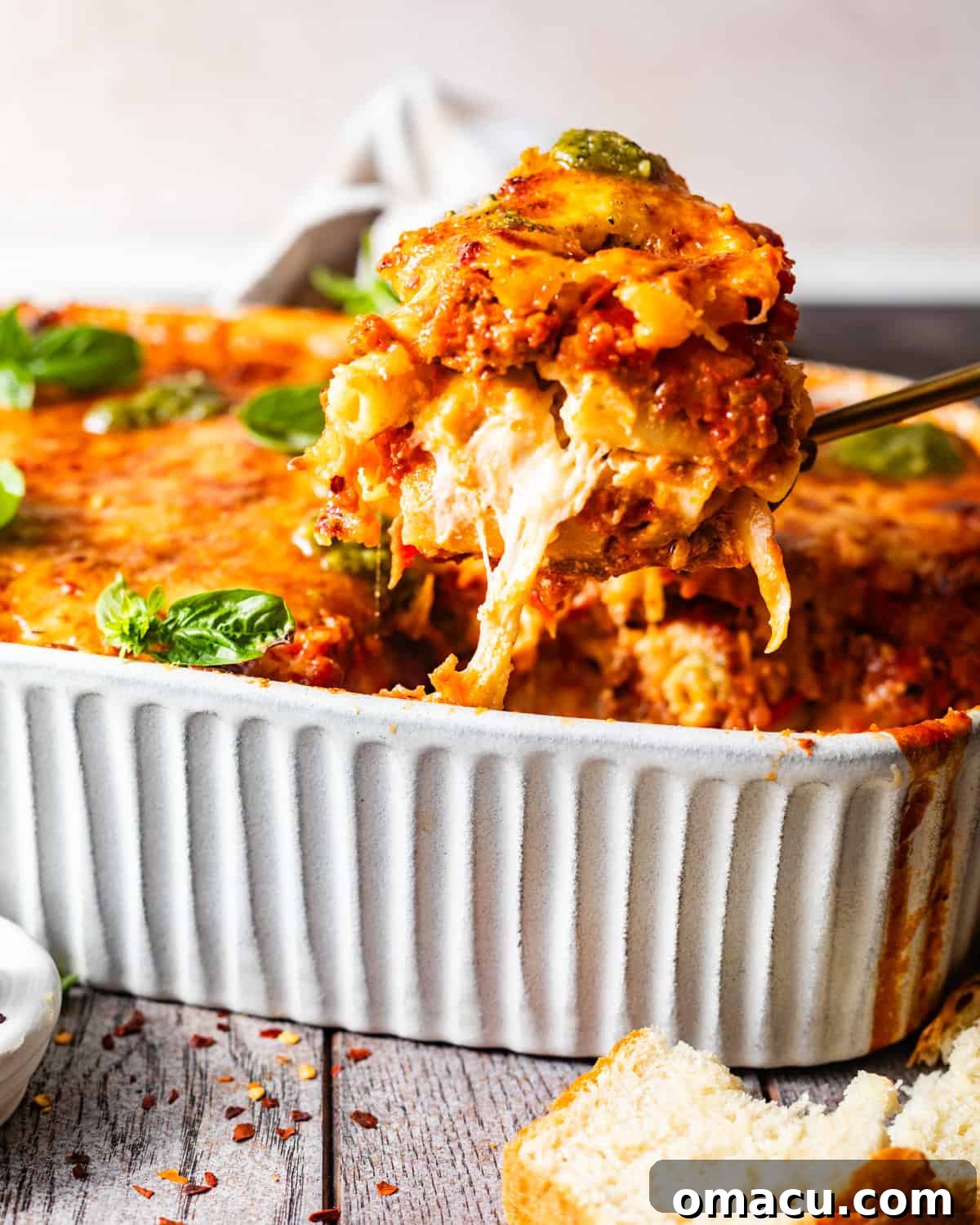 A spoon lifting a portion of baked ziti out of a baking dish, showcasing the incredible cheese pull and layers of pasta and sauce.