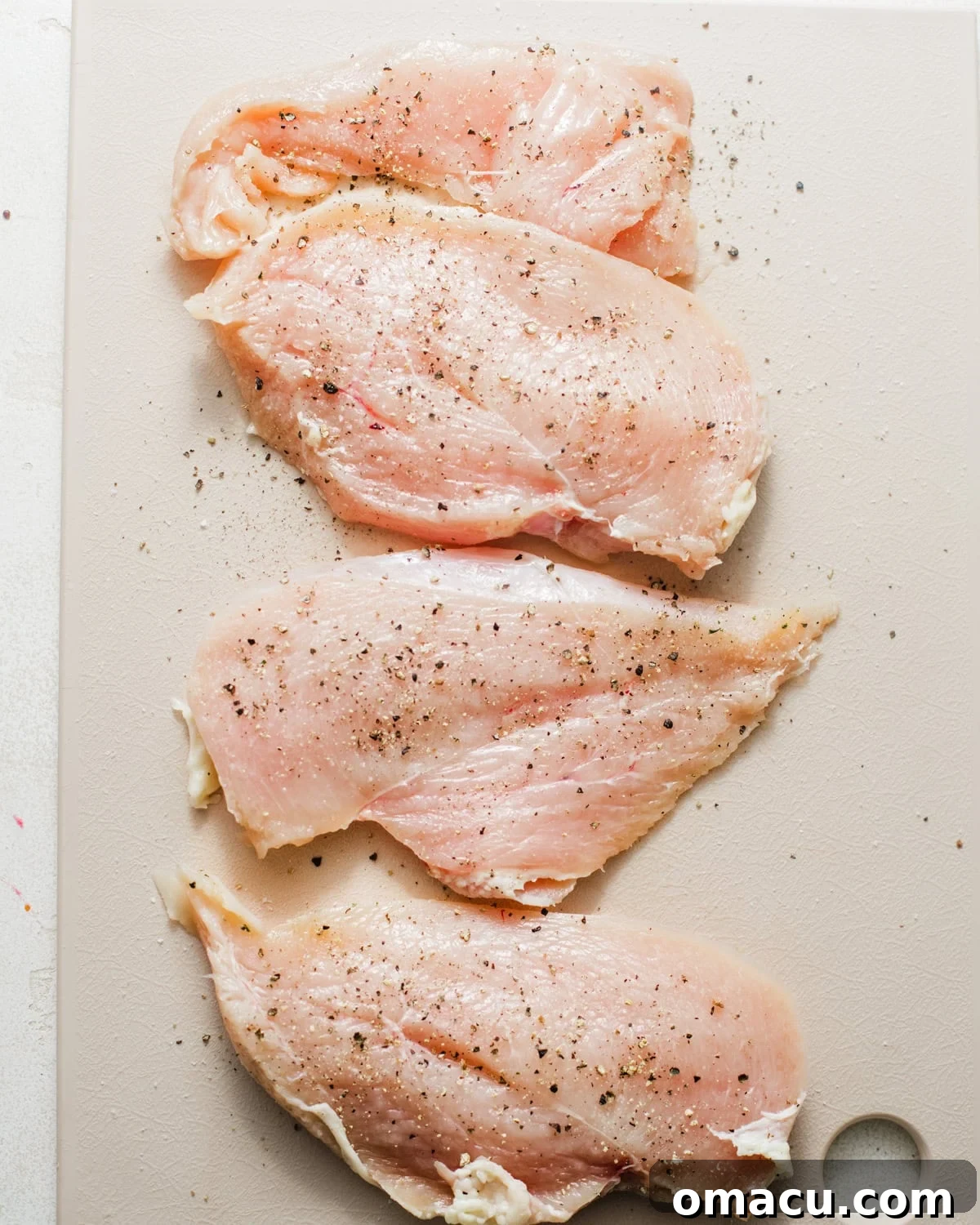 Chicken breasts on a cutting board, sliced lengthwise and seasoned with salt, pepper, and garlic powder.