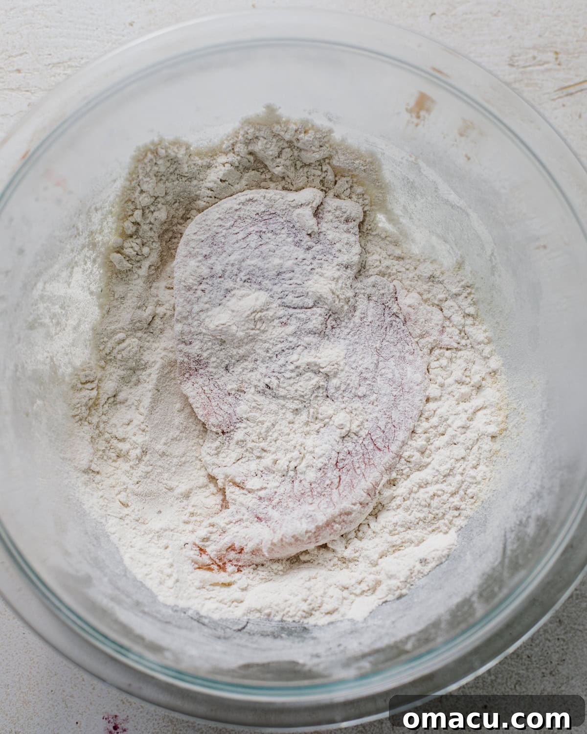 Chicken breasts being dredged in all-purpose flour in a bowl, ensuring a thorough coating.