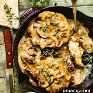 smothered pork chops in a skillet topped with fresh thyme in a mushroom and onion gravy.