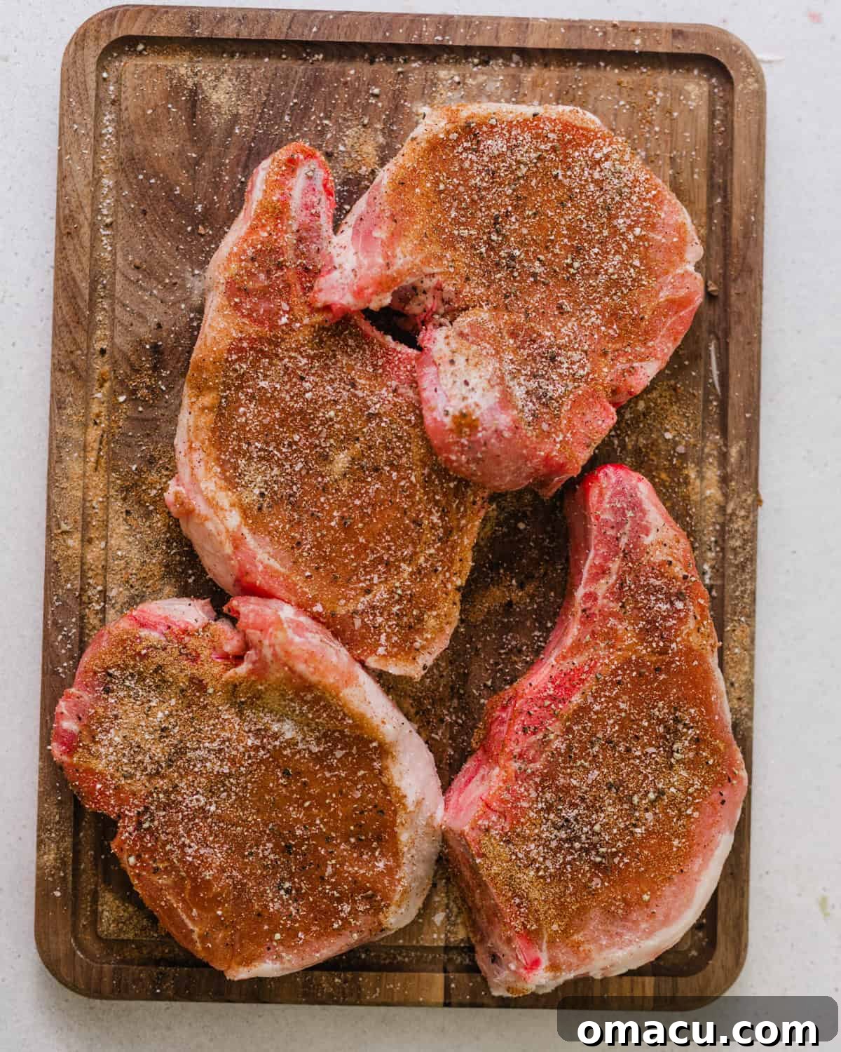 Four seasoned pork chops resting on a cutting board, coated in a dark spice blend.