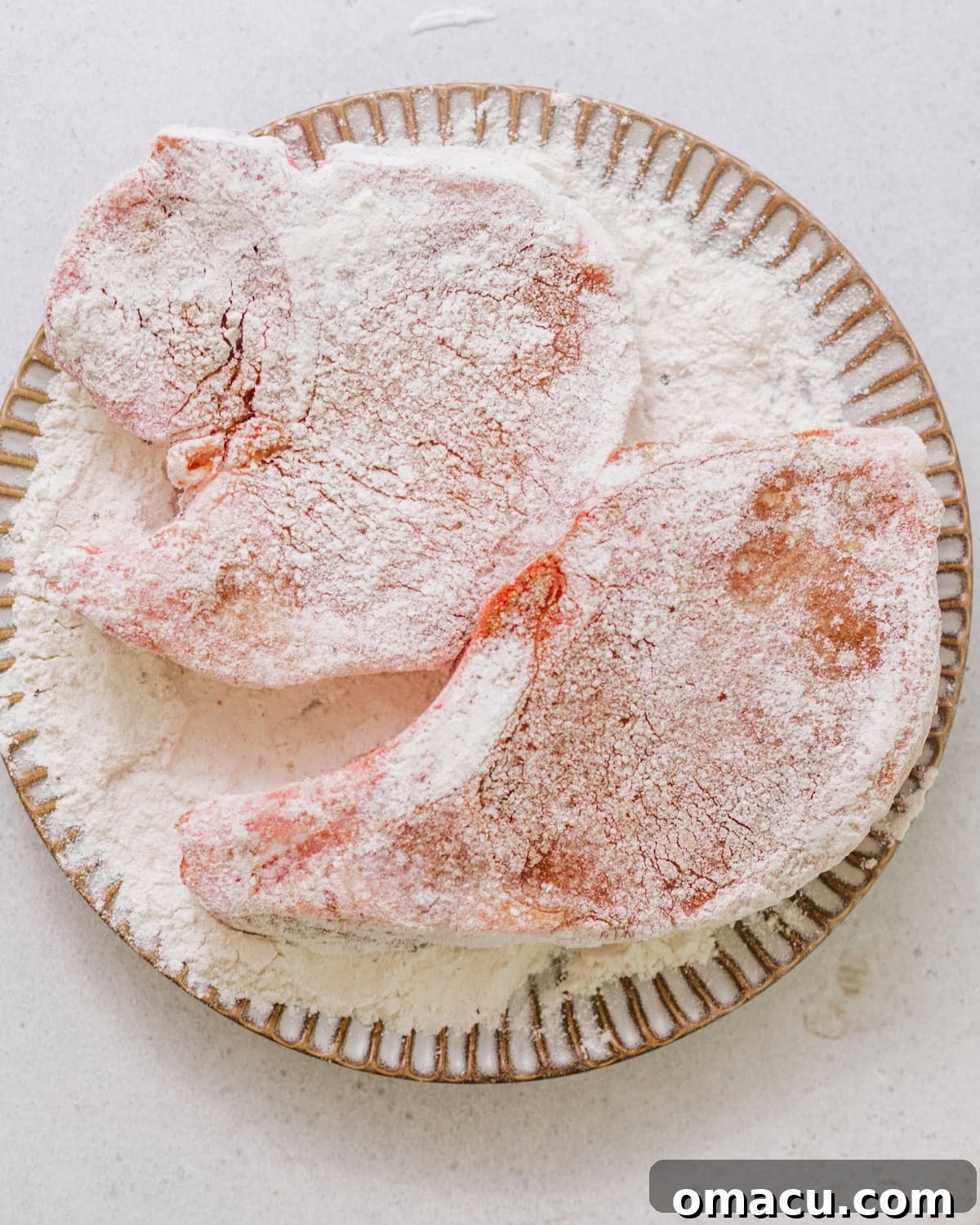 Seasoned pork chops lightly coated in flour and arranged on a plate.