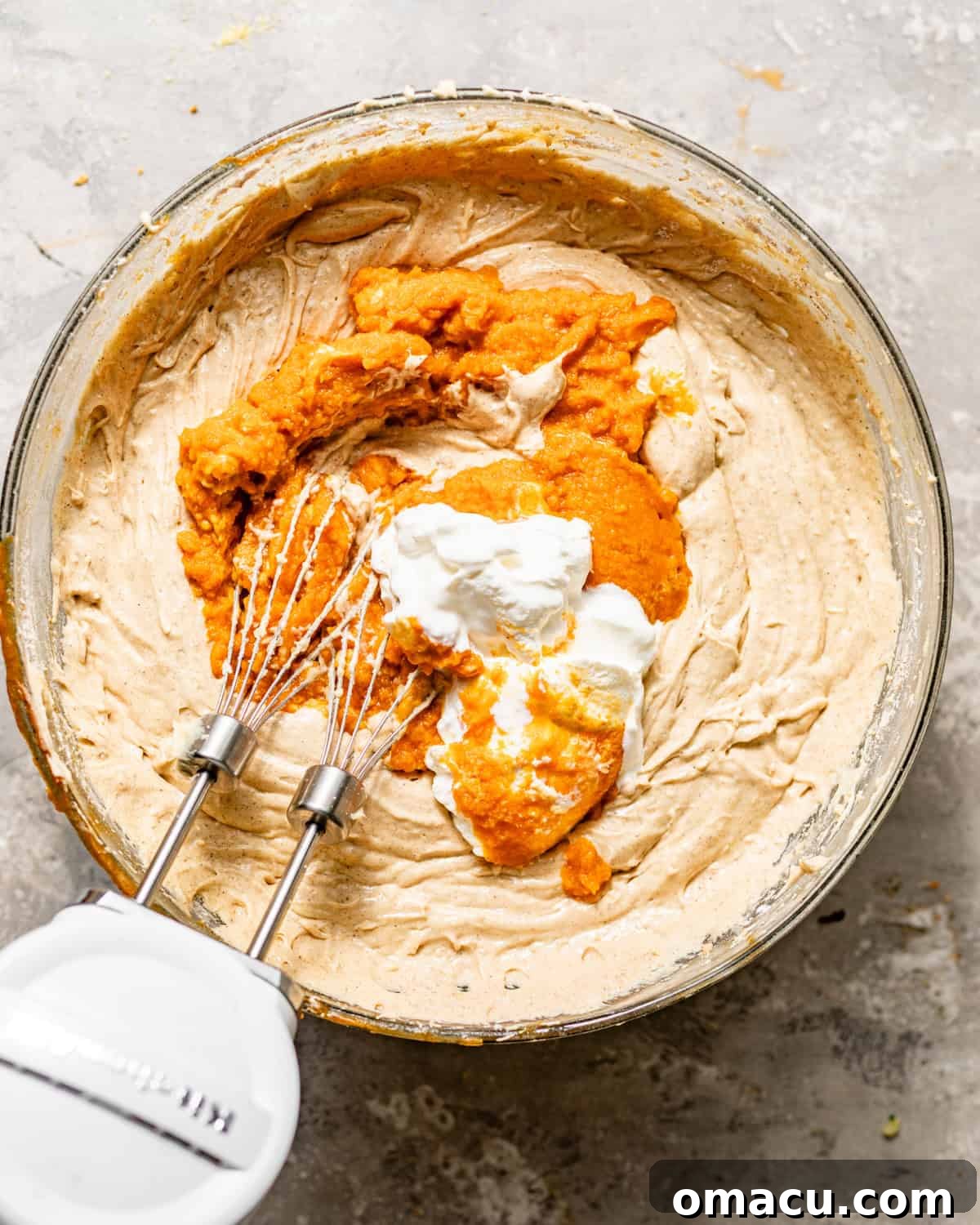 Wet ingredients for the pumpkin pound cake batter, including pumpkin puree, maple syrup, sour cream, and vanilla extract, being mixed in a bowl.