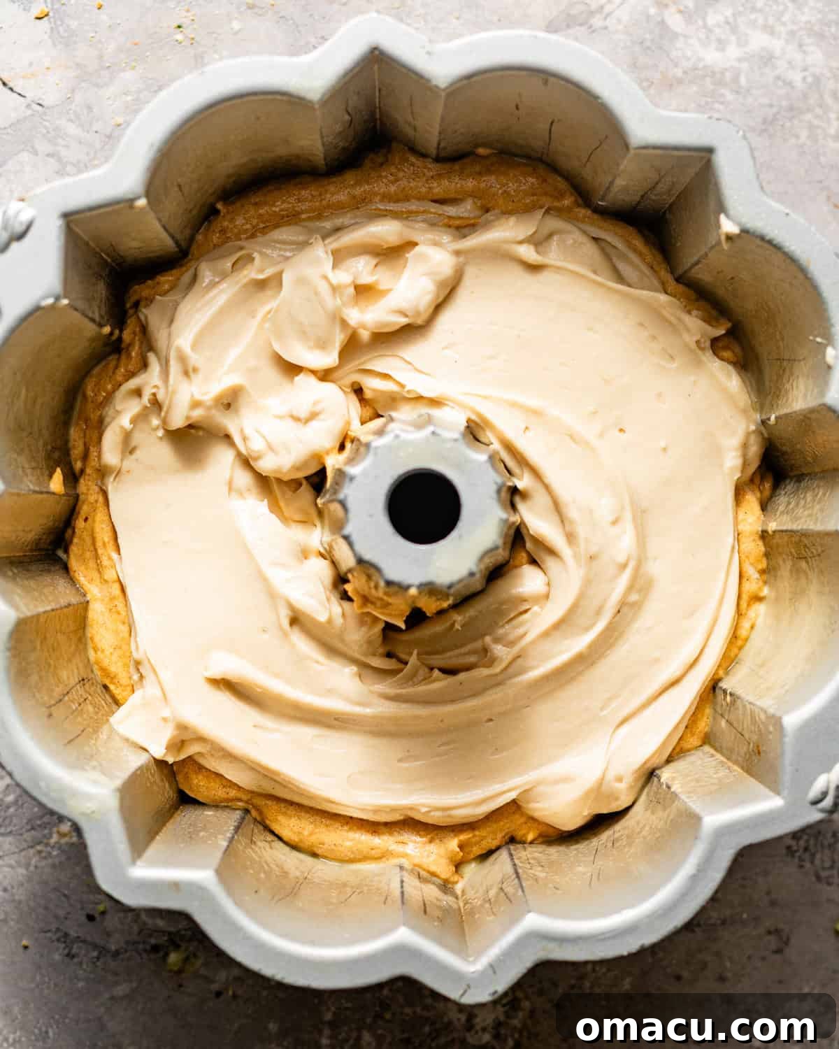 Half of the pumpkin pound cake batter carefully spread in a bundt pan, topped with the creamy white cheesecake filling, ready for the next layer of batter.