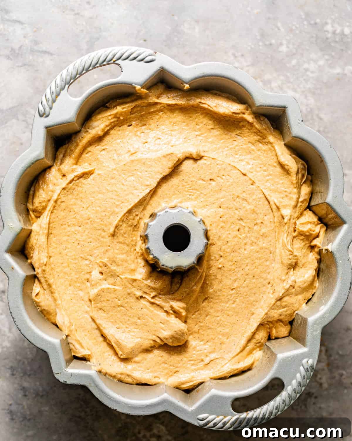 A bundt pan fully filled with pumpkin pound cake batter, smoothed over the cream cheese filling and ready for baking.