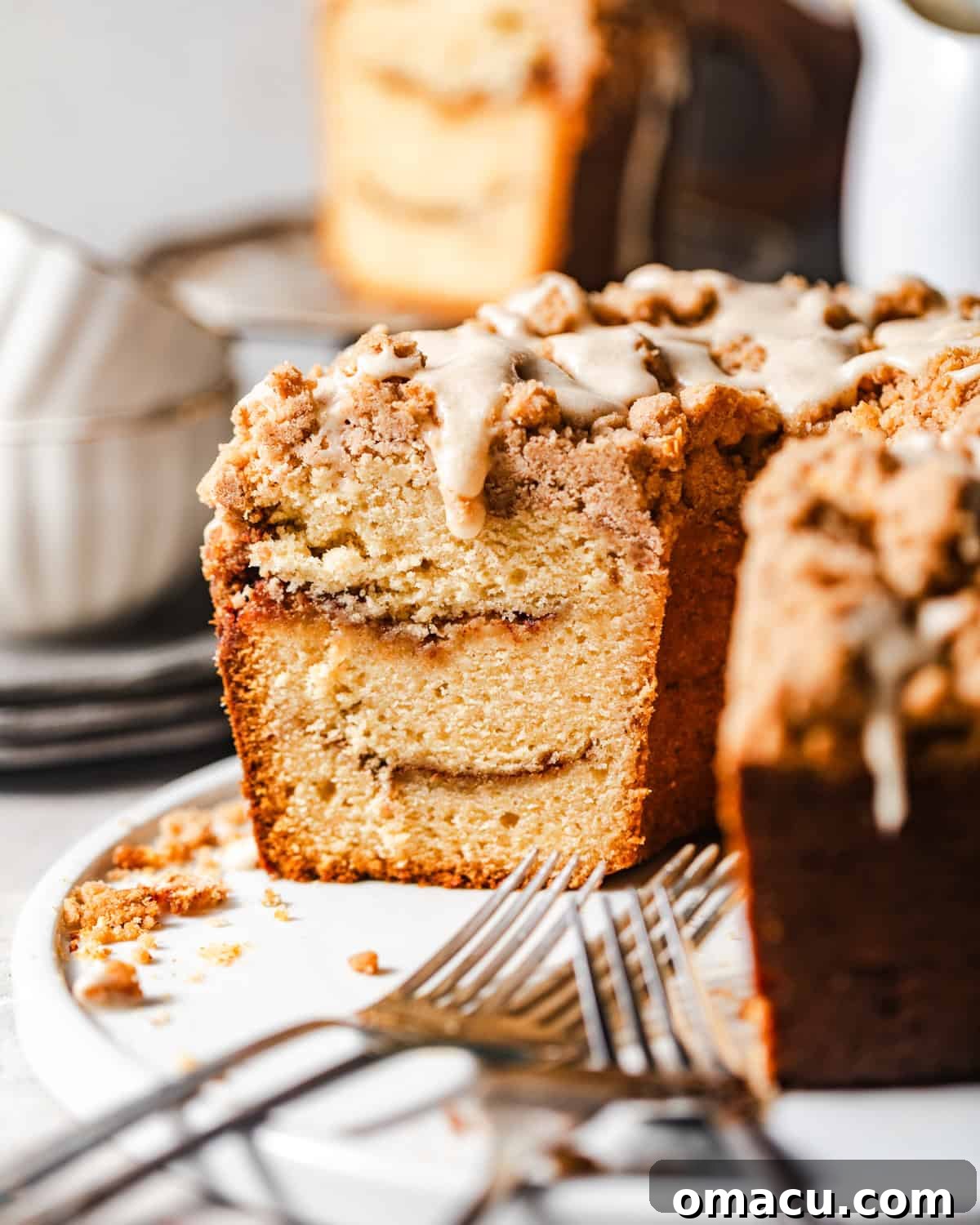 A slice of cinnamon streusel coffee cake served on a plate with forks, highlighting its moist interior and generous topping, ready for enjoyment.