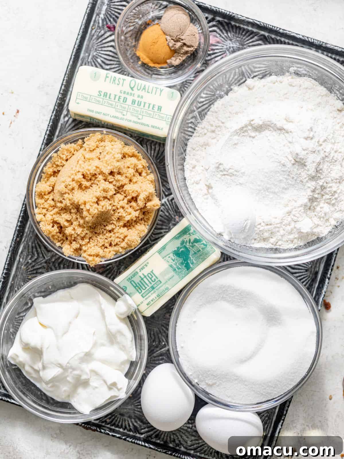 A flat lay photograph showcasing all the essential ingredients for making the Coffee Cake Bundt Cake, including all-purpose flour, brown sugar, butter, shortening, eggs, ground cinnamon, baking powder, salt, vanilla extract, whole milk, and sour cream.