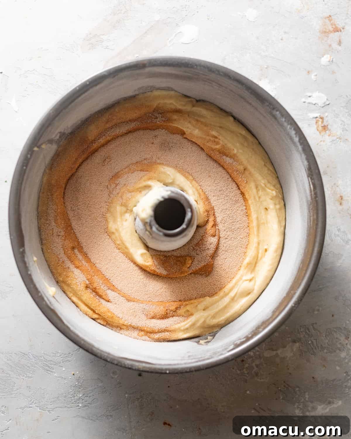 The first layer of coffee cake batter poured into a bundt pan, with cinnamon sugar filling evenly sprinkled over it, ready for the next layer.