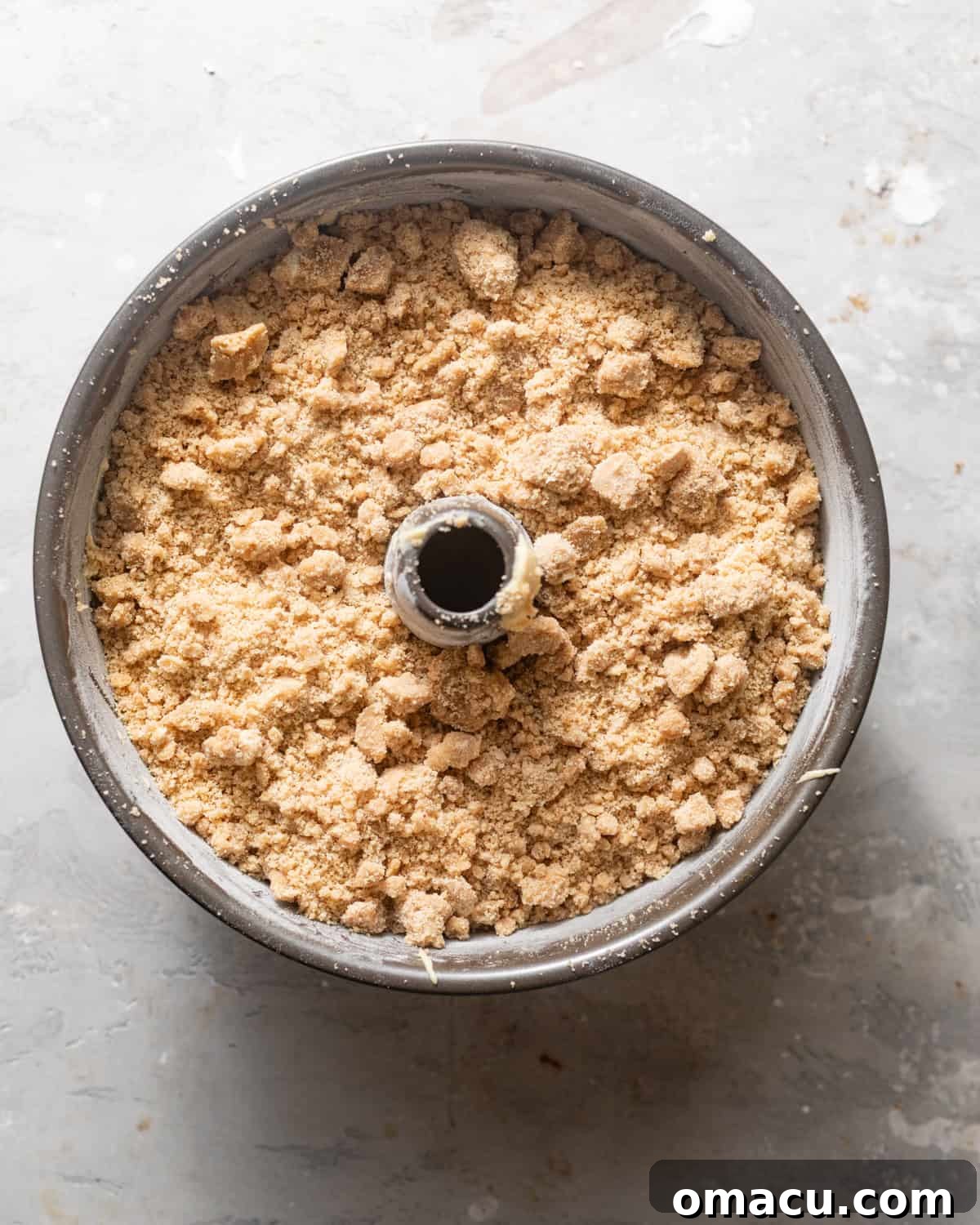 The coffee cake assembled in a tube bundt pan, with the streusel topping evenly distributed over the final layer of batter, prior to baking.