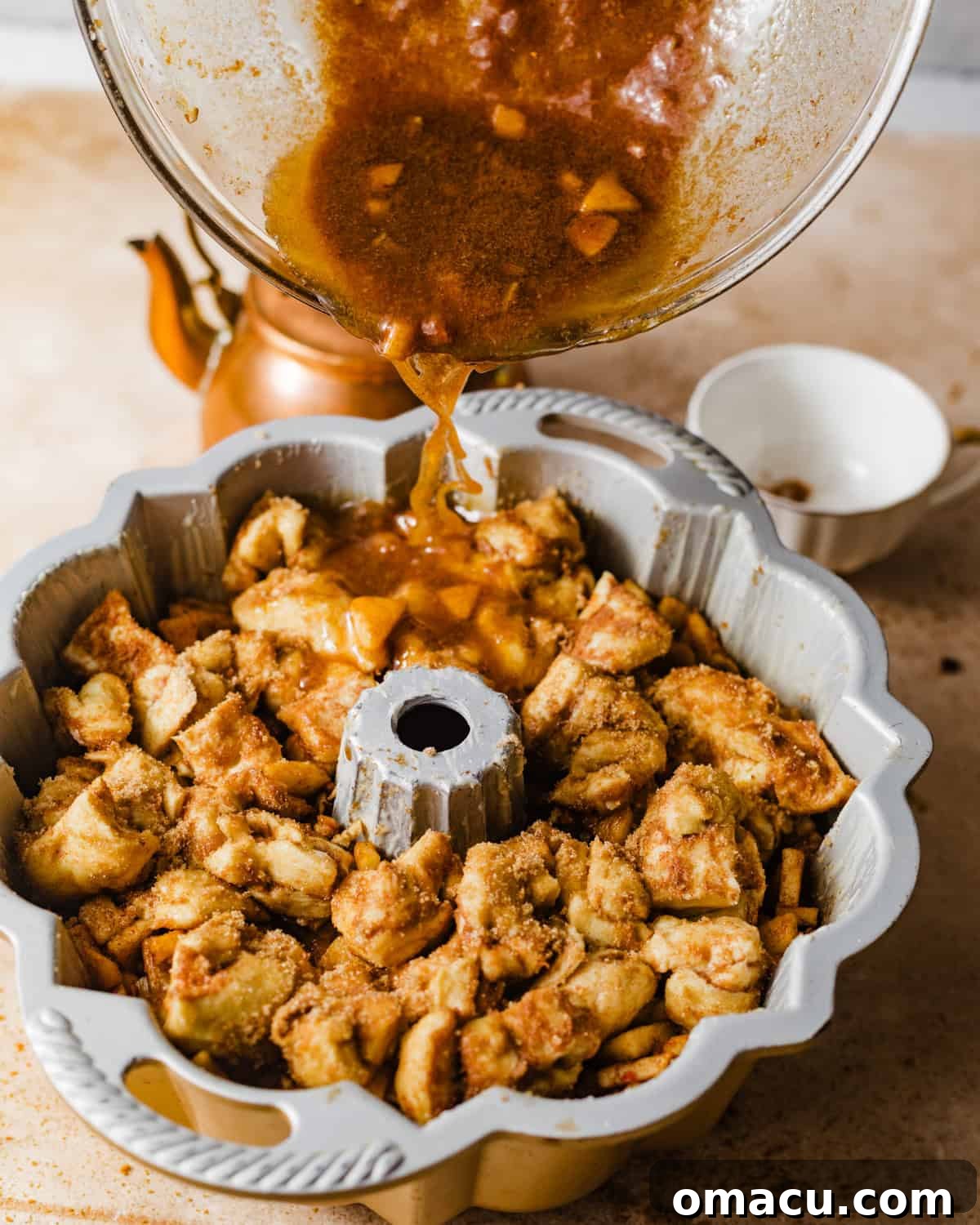 pouring the melted butter mixture on top of the apple monkey bread in the bundt pan. 