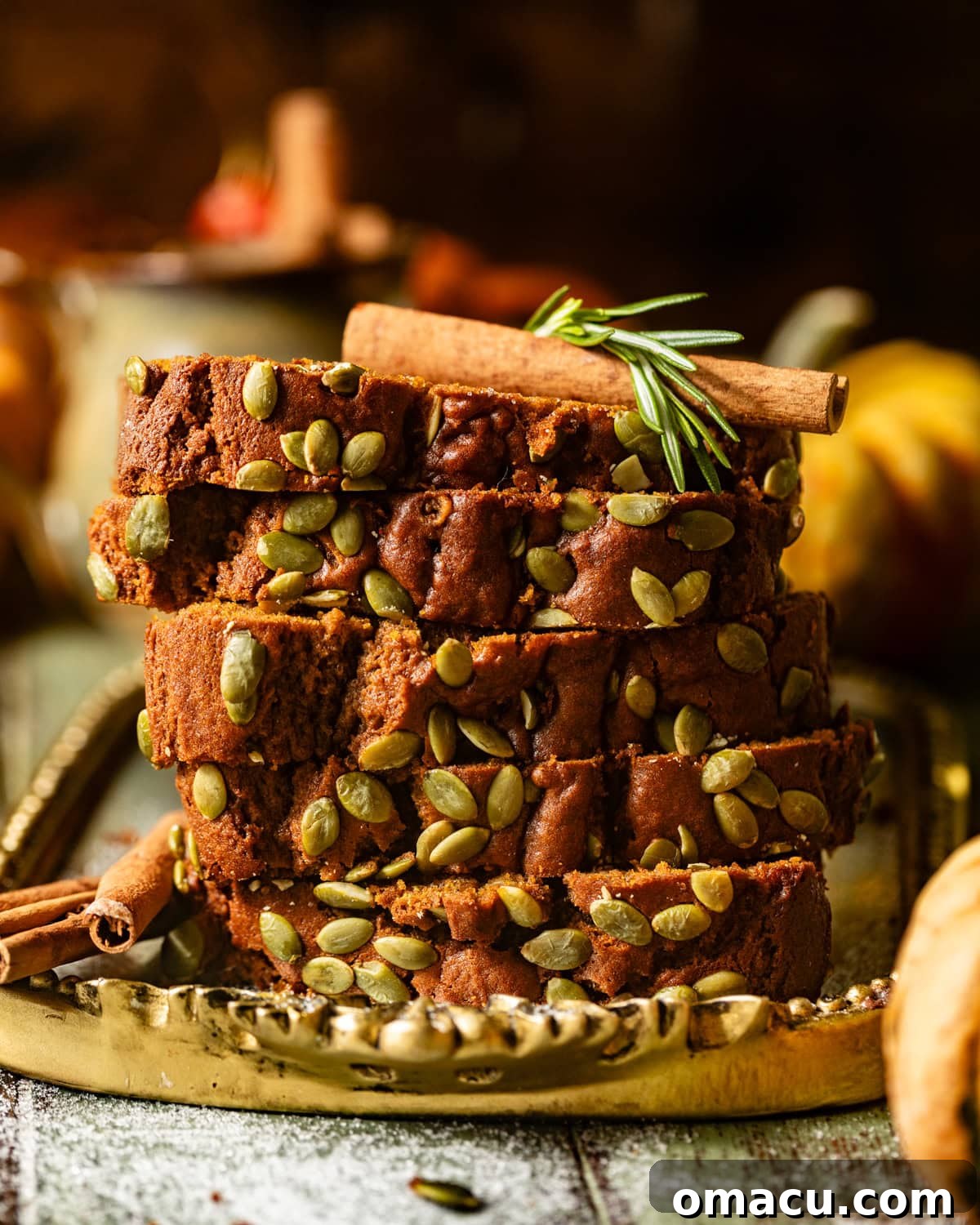 Several moist and tender slices of Starbucks copycat pumpkin bread are artfully stacked on a rustic golden plate, adorned with fragrant cinnamon sticks, highlighting the bread's inviting texture and the warm essence of autumn.