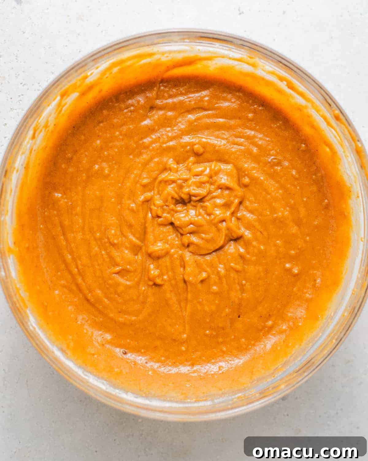 Wet ingredients, including pumpkin puree, eggs, sour cream, olive oil, melted butter, molasses, brown sugar, and granulated sugar, are vigorously whisked in a large bowl to create a smooth, unified, and creamy mixture ready for the dry components.