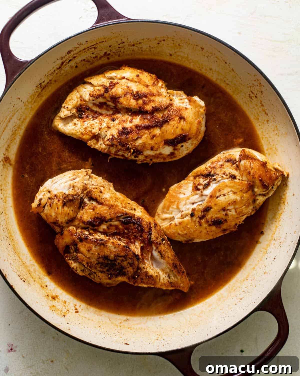 seared chicken breasts in a large pan with chicken broth being added for deglazing.