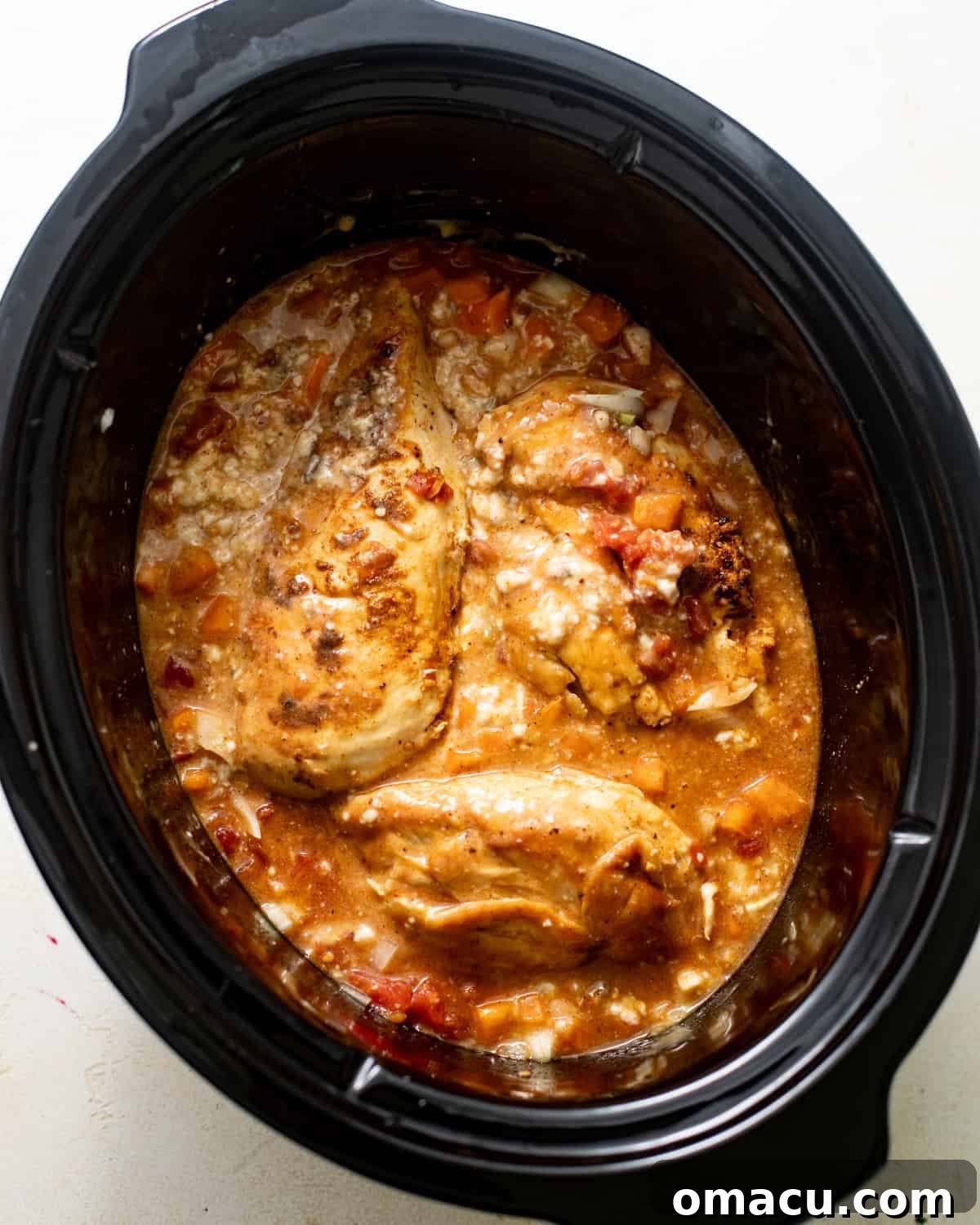 chicken breasts nestled in the slow cooker with the creamy sauce mixture, including Rotel, soups, and milk.