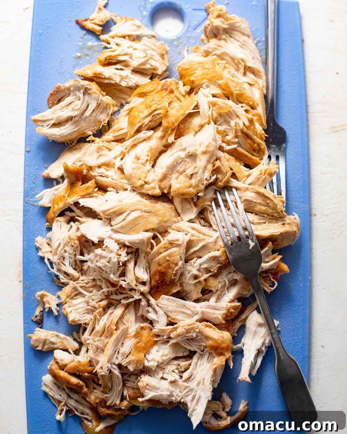 shredded chicken on a cutting board, ready to be returned to the slow cooker.