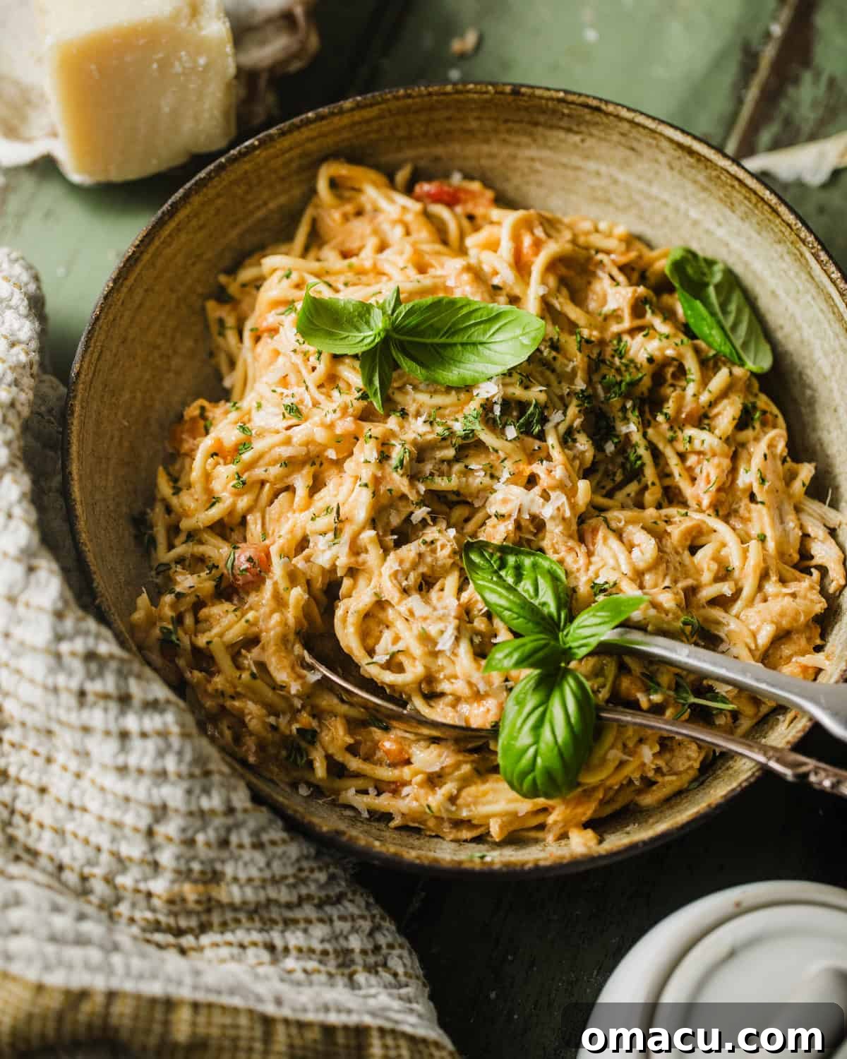 slow cooker chicken spaghetti in a bowl garnished with fresh basil and a fork ready to serve.