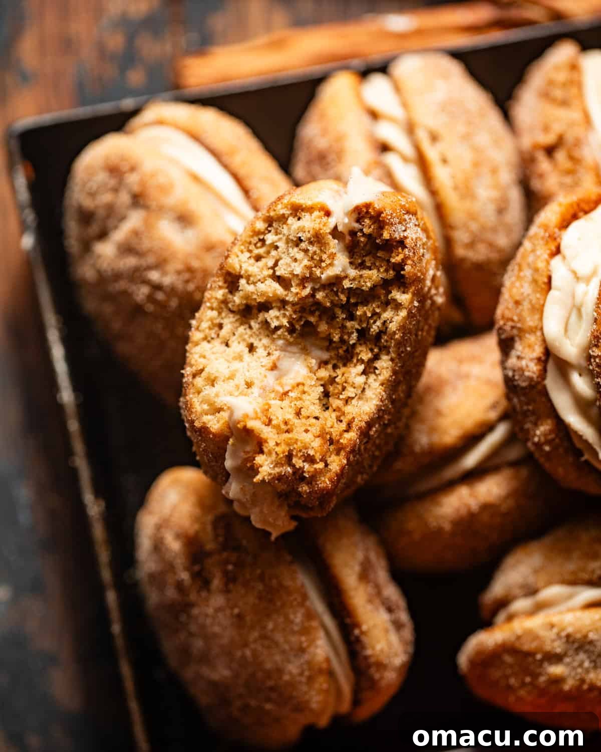 apple cider whoopie pies in a serving tray with one cookie with a bite taken out of it. 
