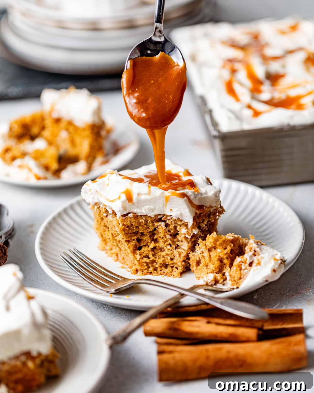 A slice of sweet potato tres leches cake on a white plate, topped with a generous dollop of cinnamon whipped cream and a glistening drizzle of salted caramel, invitingly ready to be enjoyed.