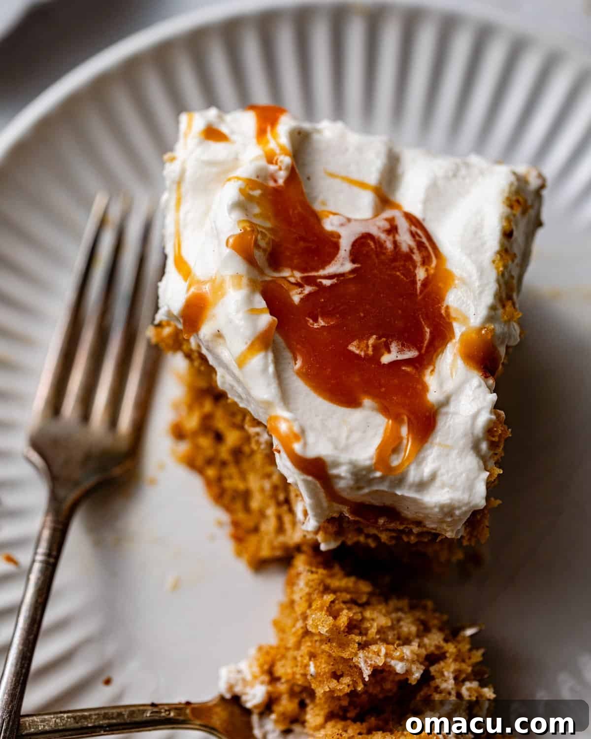 A delectable slice of sweet potato tres leches cake, adorned with fluffy whipped cream and a luxurious drizzle of salted caramel, captured up close with a fork poised to enjoy.