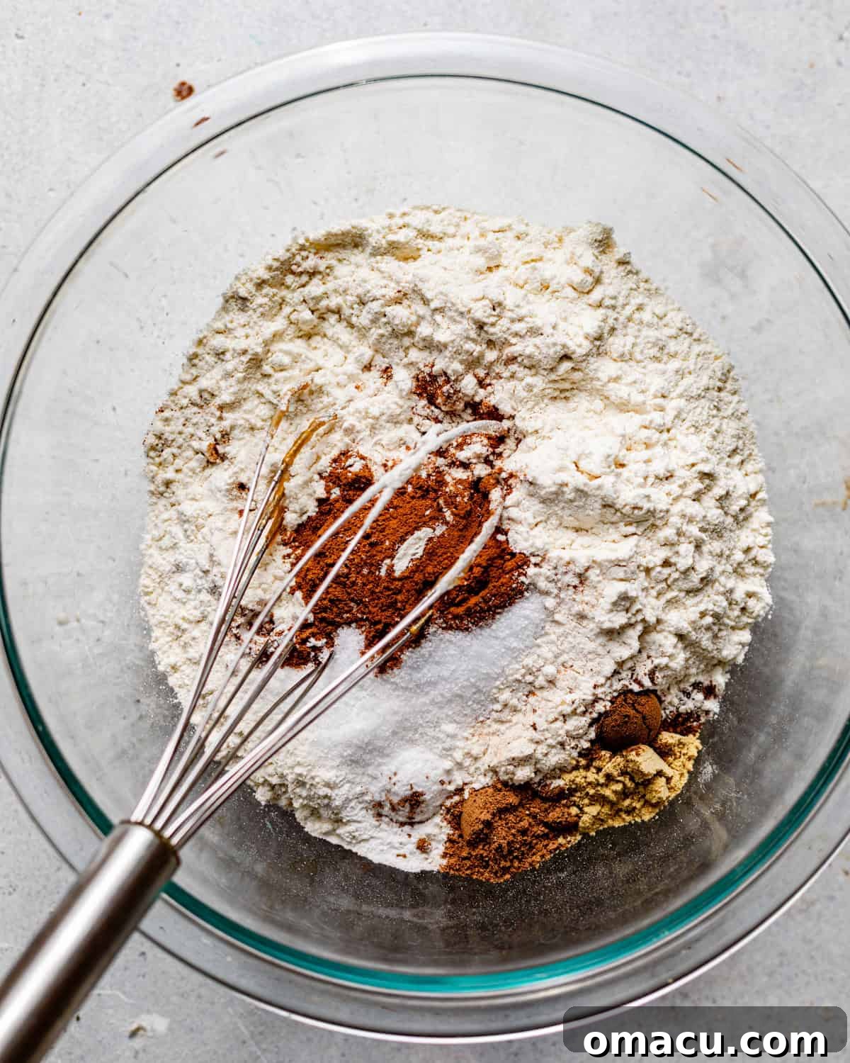 Wet ingredients (sweet potato puree, oil, sugars, buttermilk, and vanilla) are being whisked in a large bowl, creating a smooth, creamy base before eggs are added.