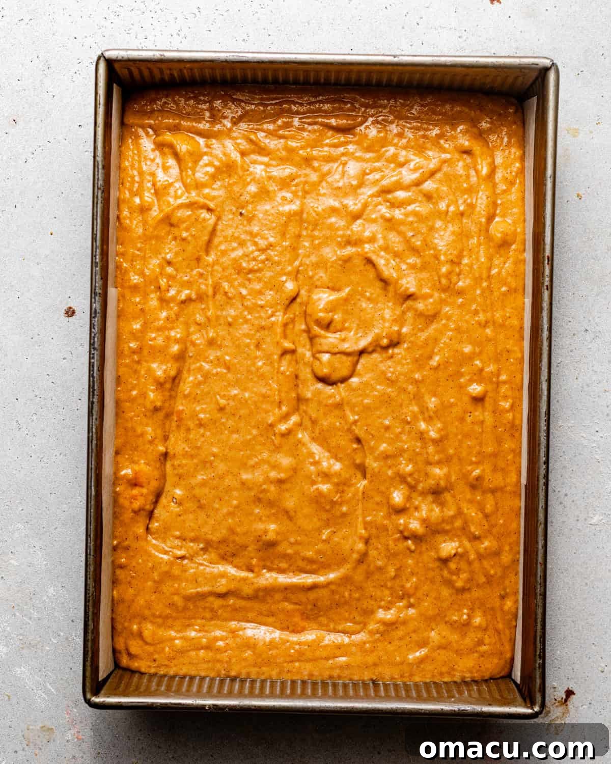 Sweet potato cake batter smoothly poured into a parchment-lined 9x13 inch baking dish, ready for baking.