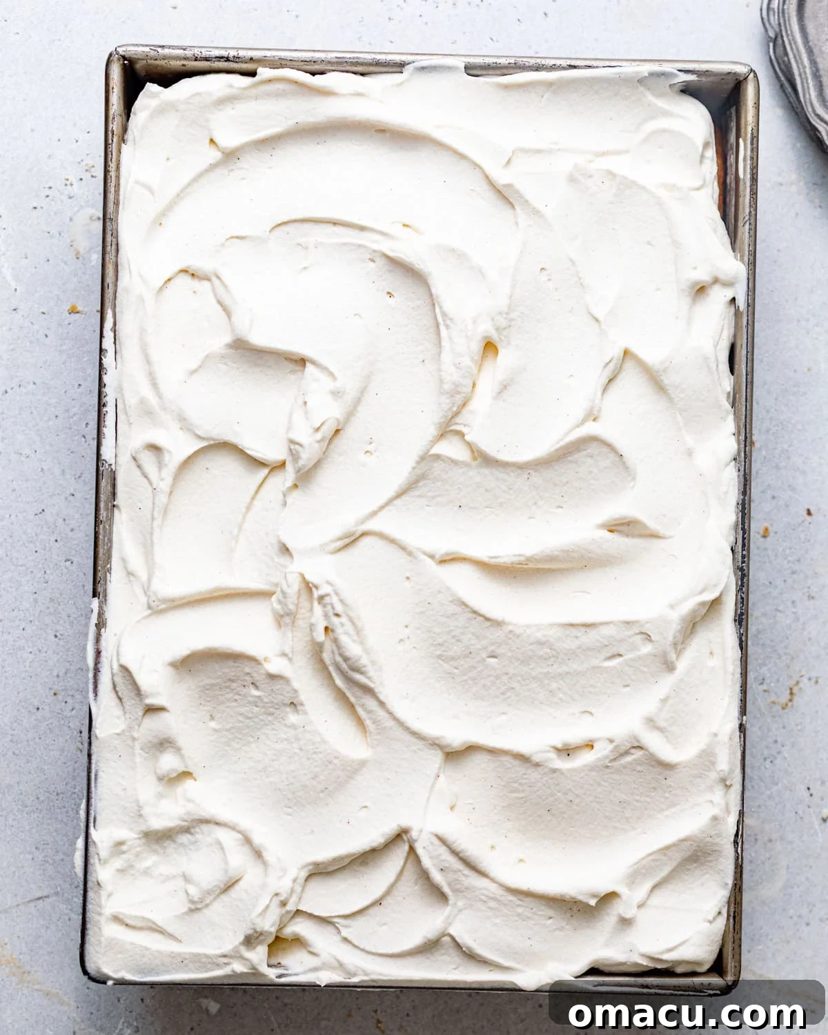 A beautifully frosted sweet potato tres leches cake in a baking dish, topped with a thick layer of cinnamon whipped cream, ready for final garnishing.