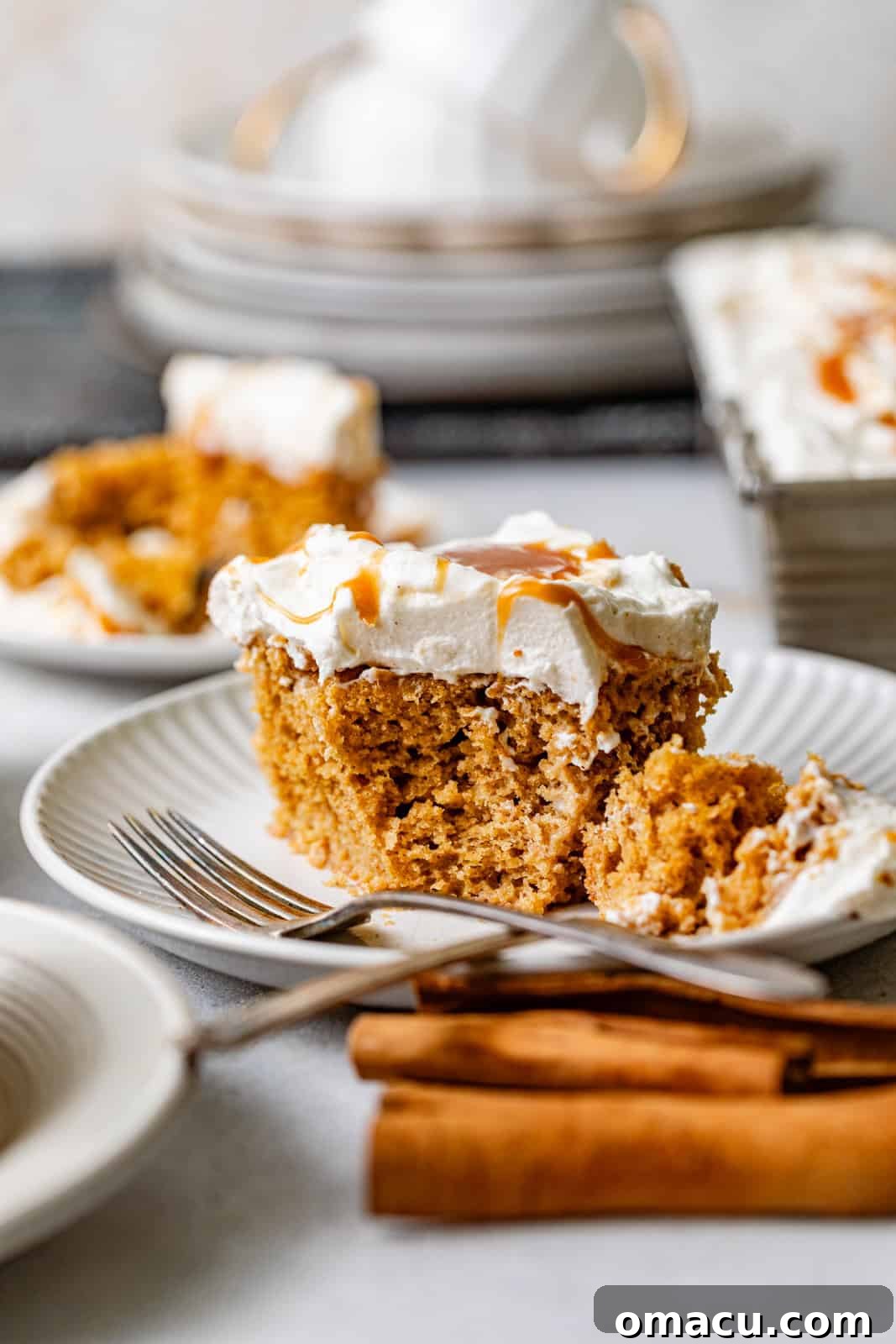 An enticing close-up shot of a slice of sweet potato tres leches cake on a plate, showcasing its moist texture, topped with fluffy cream and caramel, with a fork ready to scoop a bite.