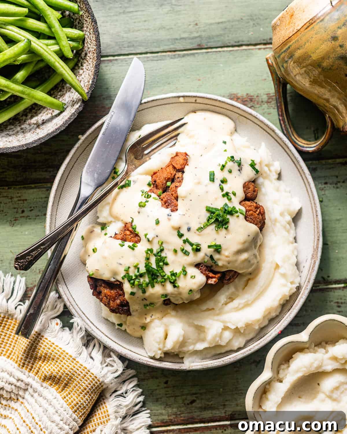 An inviting overhead view of chicken fried steak with gravy, accompanied by a side of fluffy mashed potatoes and vibrant green beans in a bowl.
