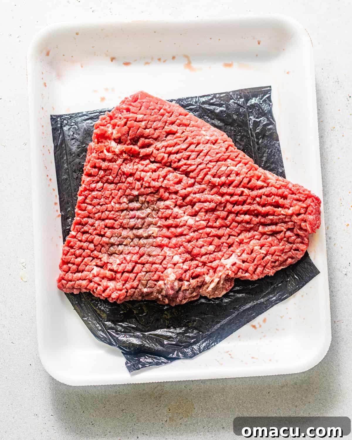 Pounded cube steak laid flat on a white cutting surface, showing its tenderized, even thickness.