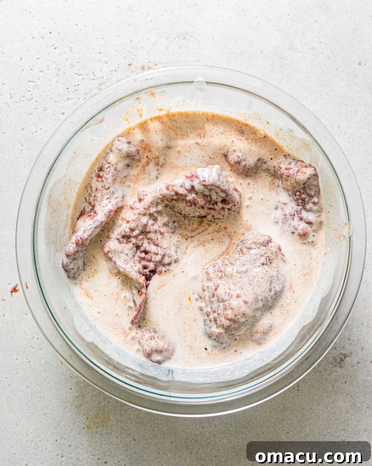 Pounded cube steaks soaking in a flavorful buttermilk marinade in a large glass bowl, ready for absorption.