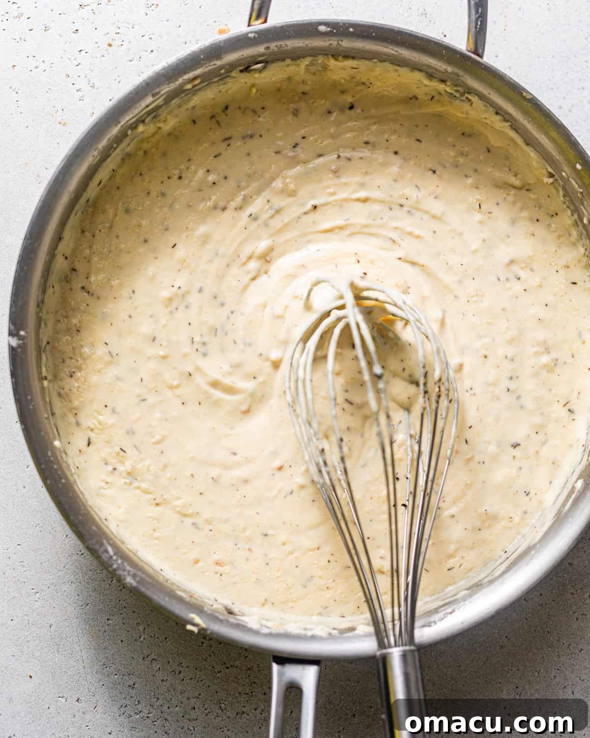 Creamy white pepper gravy simmering in a skillet, being whisked to perfect, smooth consistency.