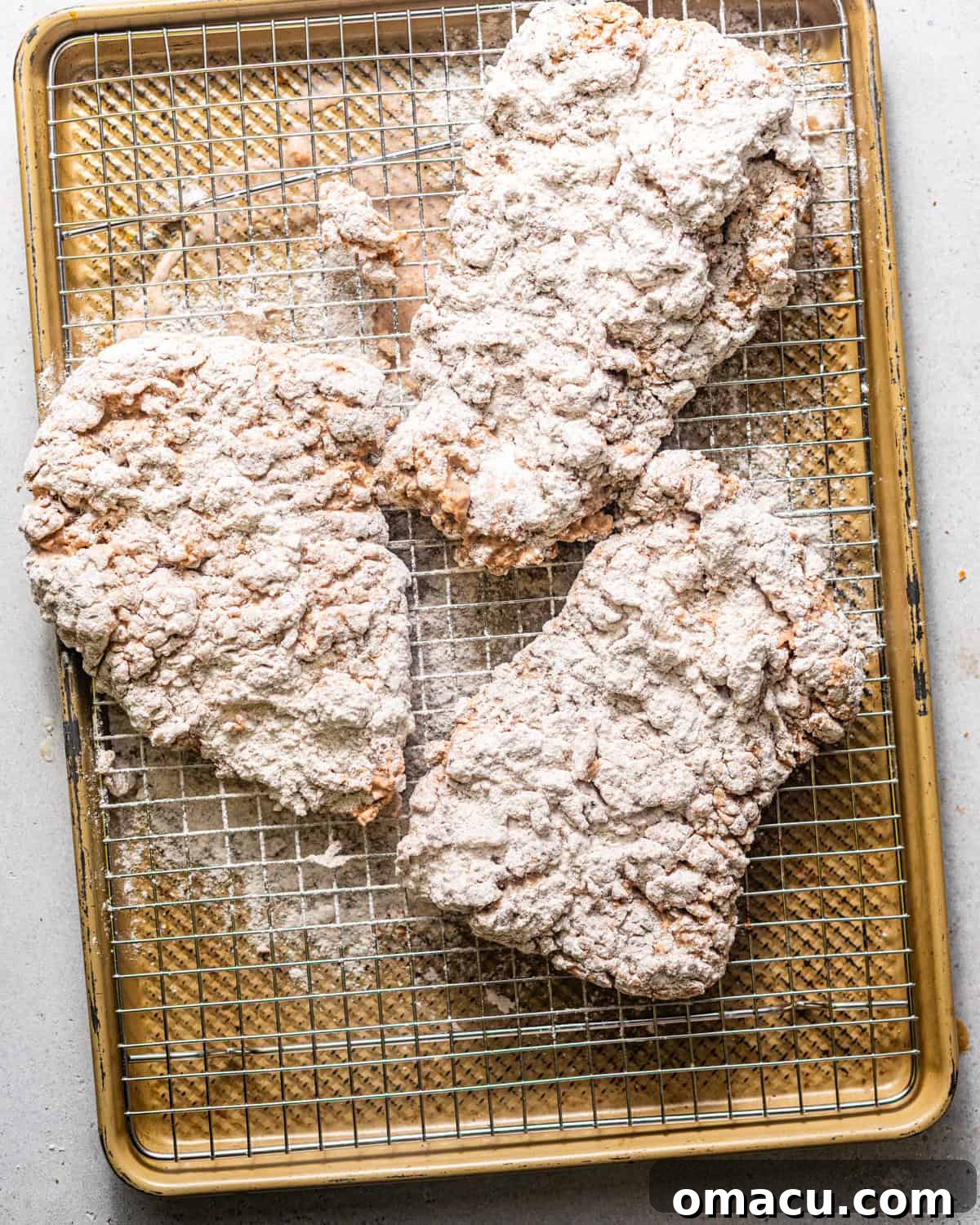 Breaded cube steaks resting on a wire rack, allowing the coating to set before frying, ensuring maximum crispness.