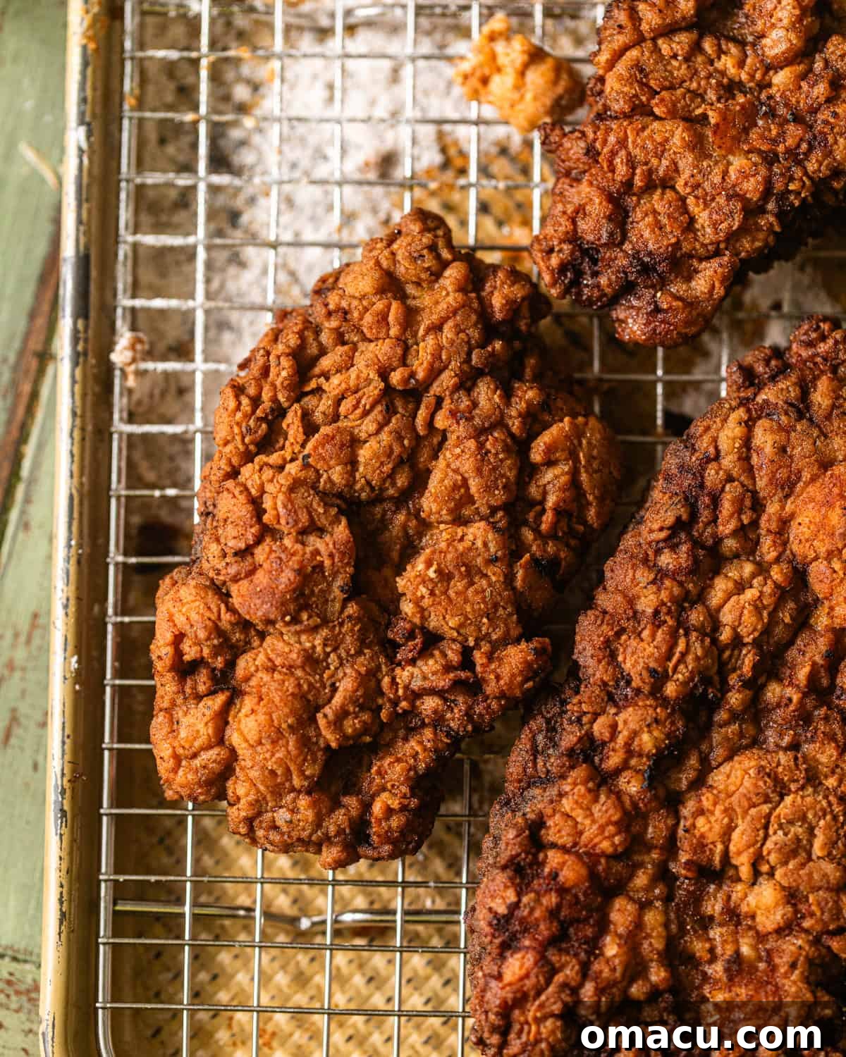 Freshly fried chicken fried steak, golden brown and crispy, draining excess oil on a wire rack.