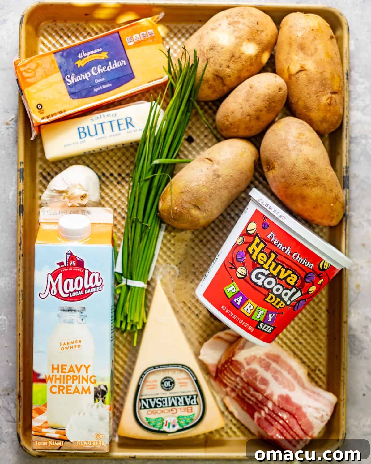 Ingredients laid out for twice baked mashed potatoes: potatoes, cheddar cheese, heavy cream, French onion dip, Parmesan cheese, bacon, chives, butter, and various seasonings.