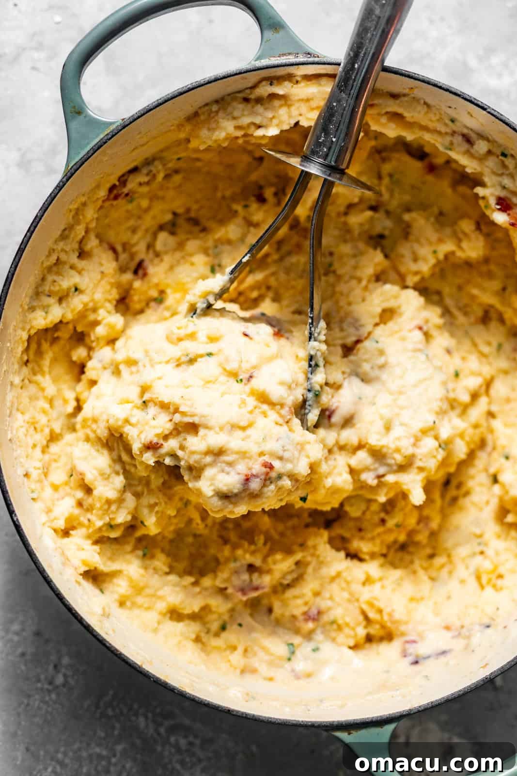 Creamy mashed potatoes being mixed in a large pot with French onion dip, shredded cheese, heavy cream, and various seasonings.