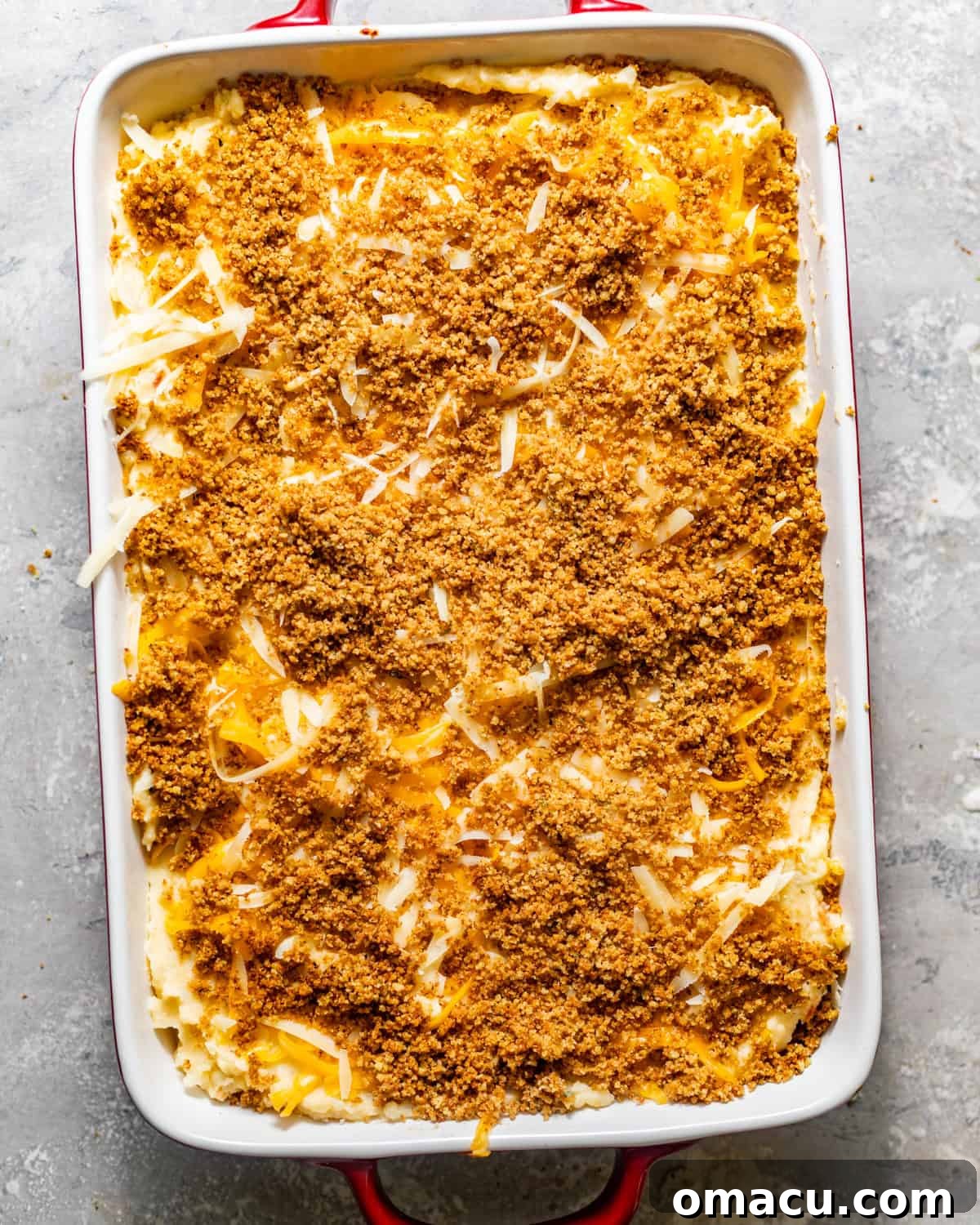 Assembled twice baked mashed potatoes in a 9x13 baking dish, topped with breadcrumbs and cheese, ready for the oven.