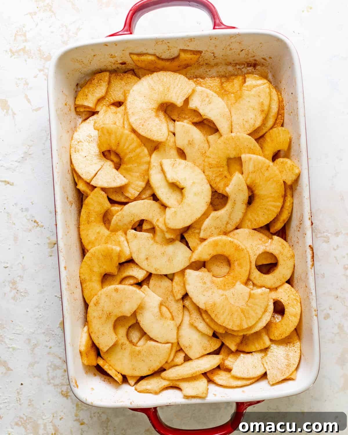 Sliced Honeycrisp apples are generously tossed with cinnamon, brown sugar, cornstarch, and a touch of lemon juice in a baking dish.