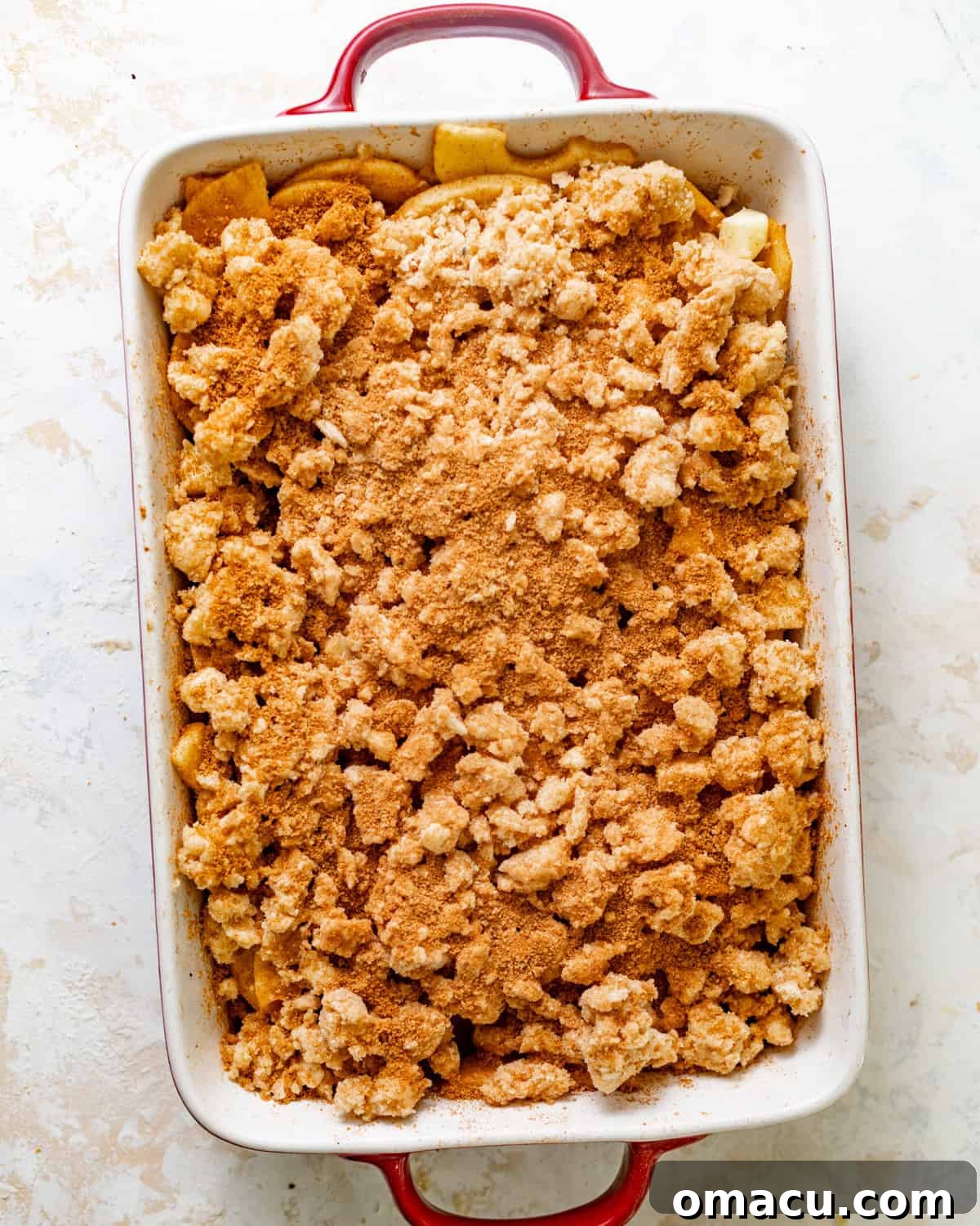 The apple cobbler, assembled in a baking dish, with the biscuit topping generously sprinkled with cinnamon sugar before baking.