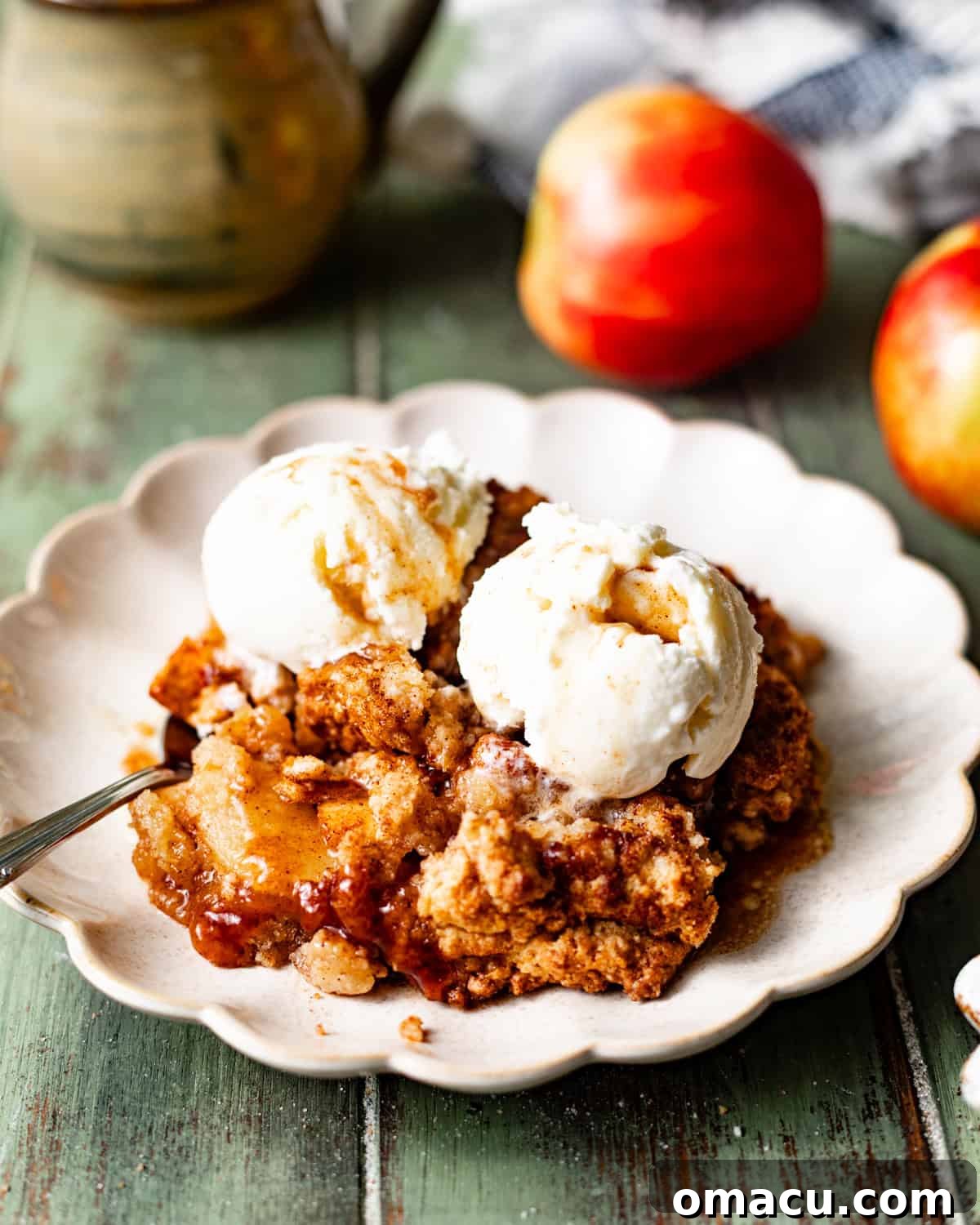 A plate holding a serving of warm apple cobbler with a scoop of melting ice cream and a spoon, inviting a taste.