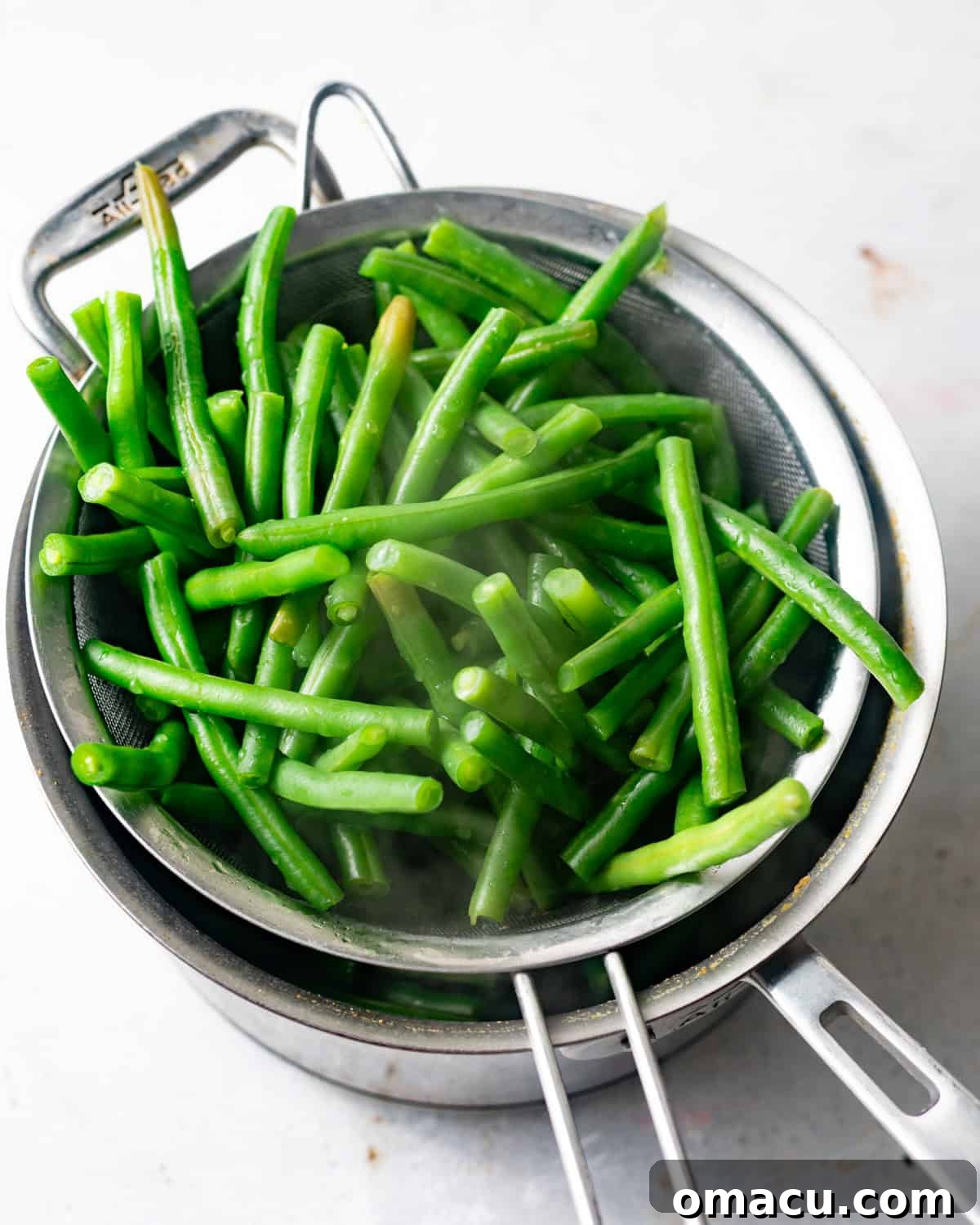Blanched green beans resting in a sieve, draining over a saucepan, their vibrant green color preserved.