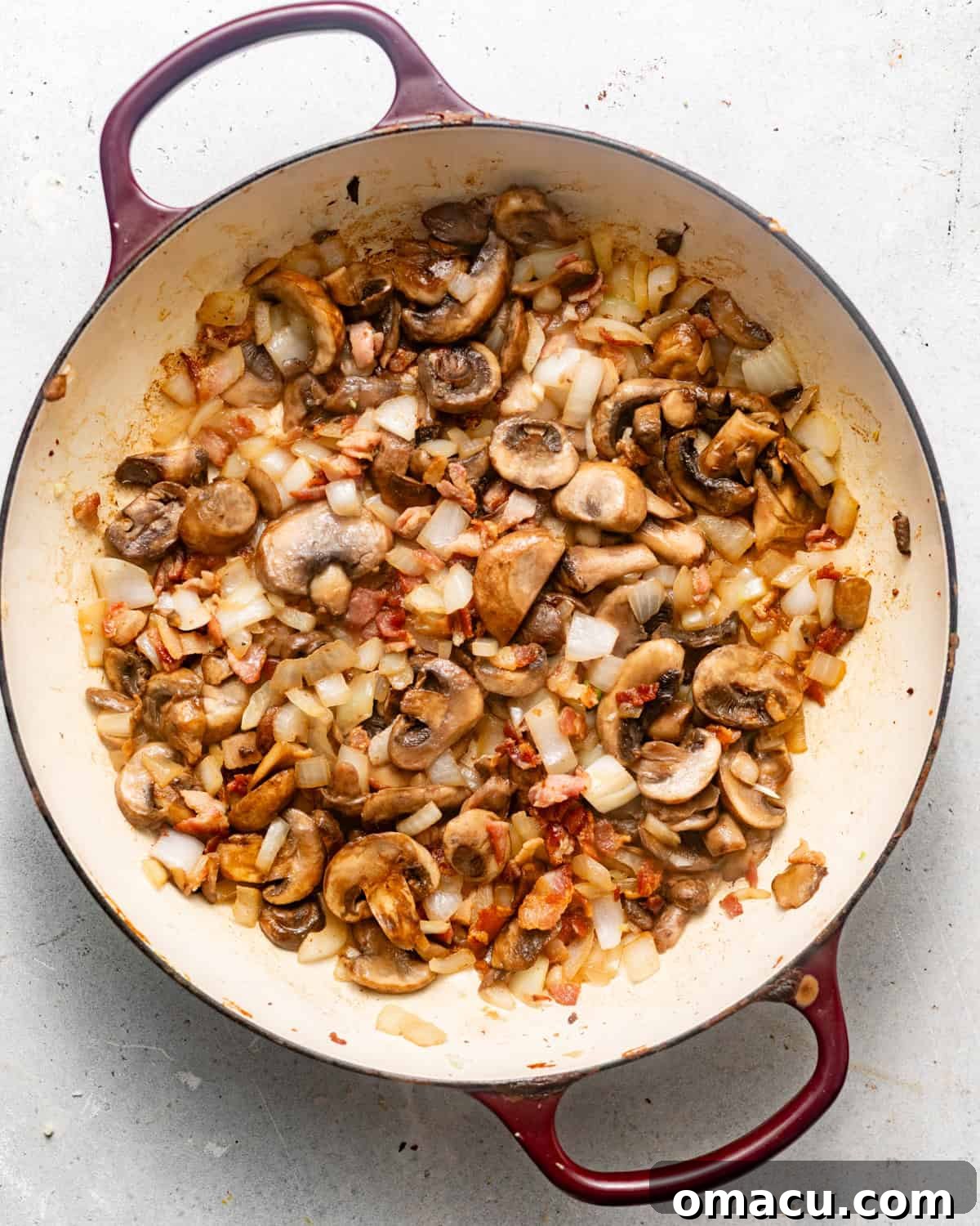 A mix of cooked bacon, diced onions, and sliced mushrooms sautéing together in a large pan, creating a rich aromatic base.