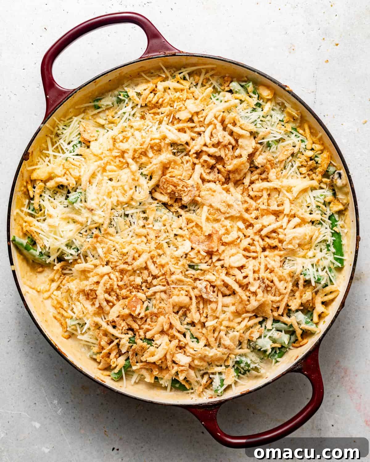 The assembled green bean casserole in a large 9x13 baking dish, generously topped with crispy fried onions and a final sprinkle of Parmesan cheese, ready for baking.
