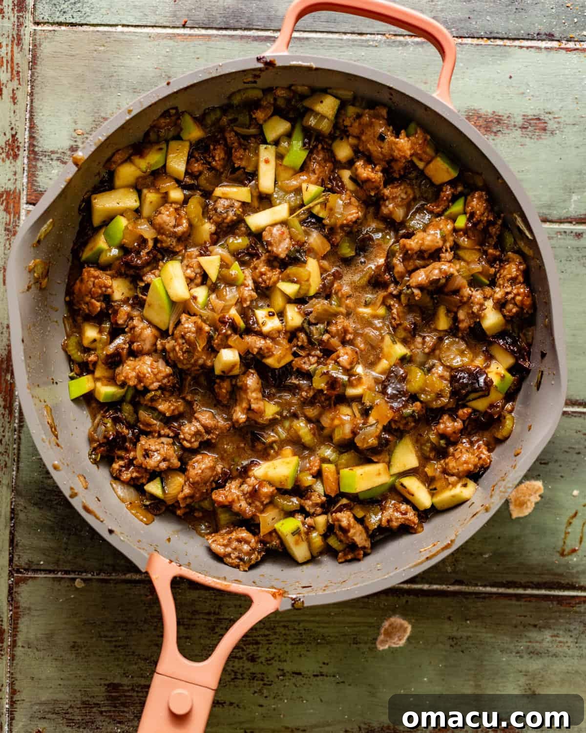 Sausage mixture simmering in a large skillet with prunes, fresh herbs, onions, celery, apples, and pecans.
