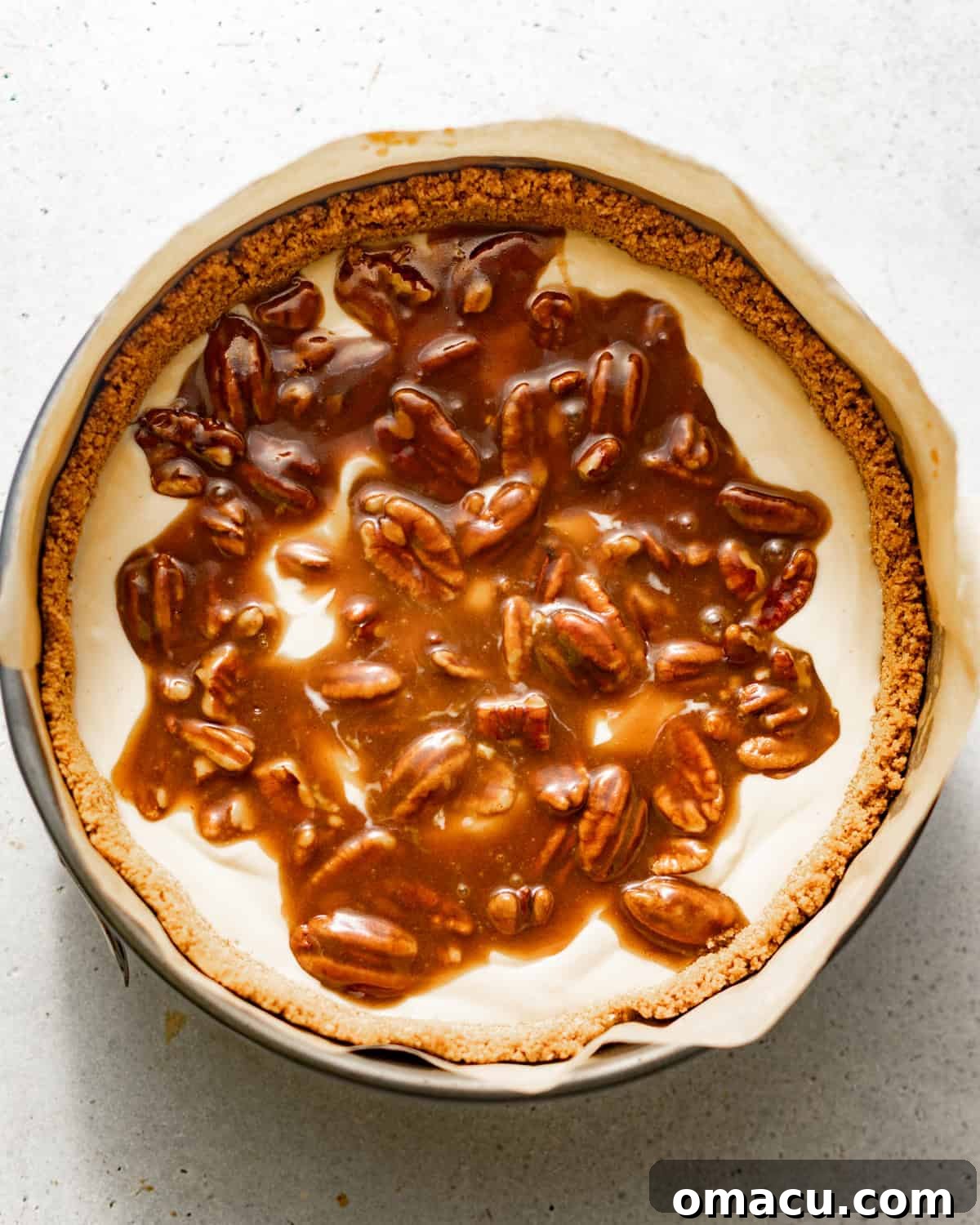 Half of the creamy cheesecake batter poured into the springform pan, with a generous layer of pecan pie filling nestled in the middle.