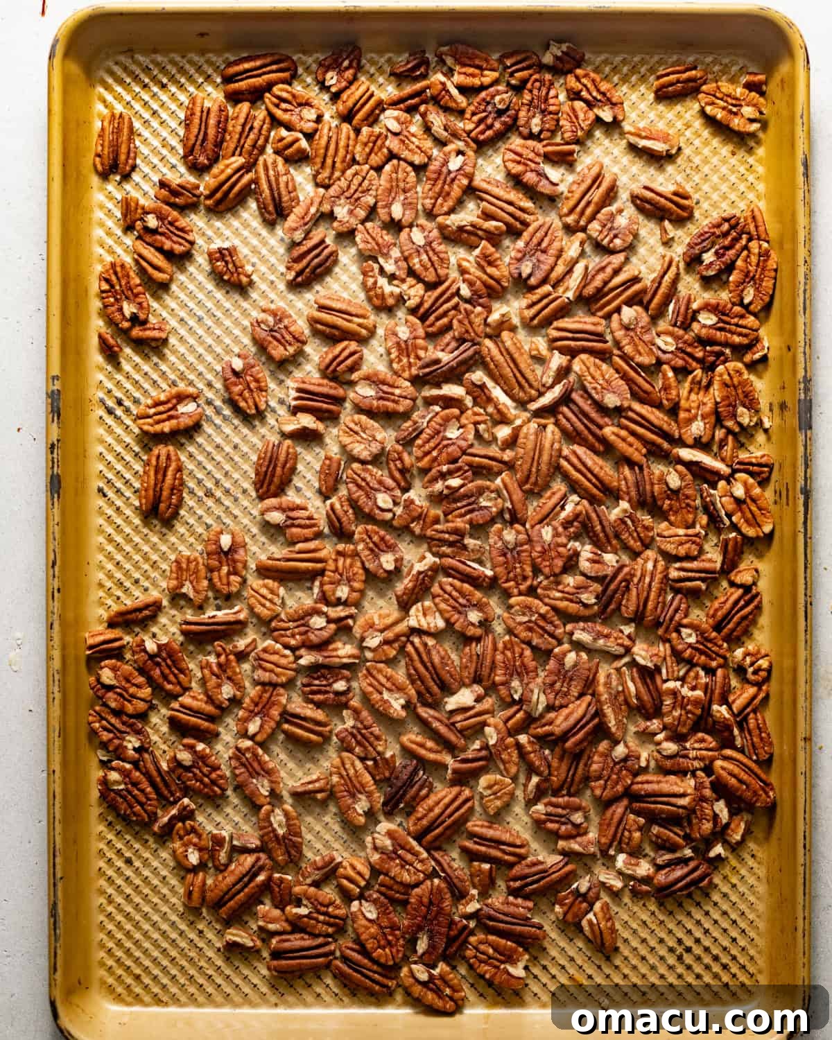 Toasted pecans evenly spread on a baking sheet, ready to be incorporated into the recipe.