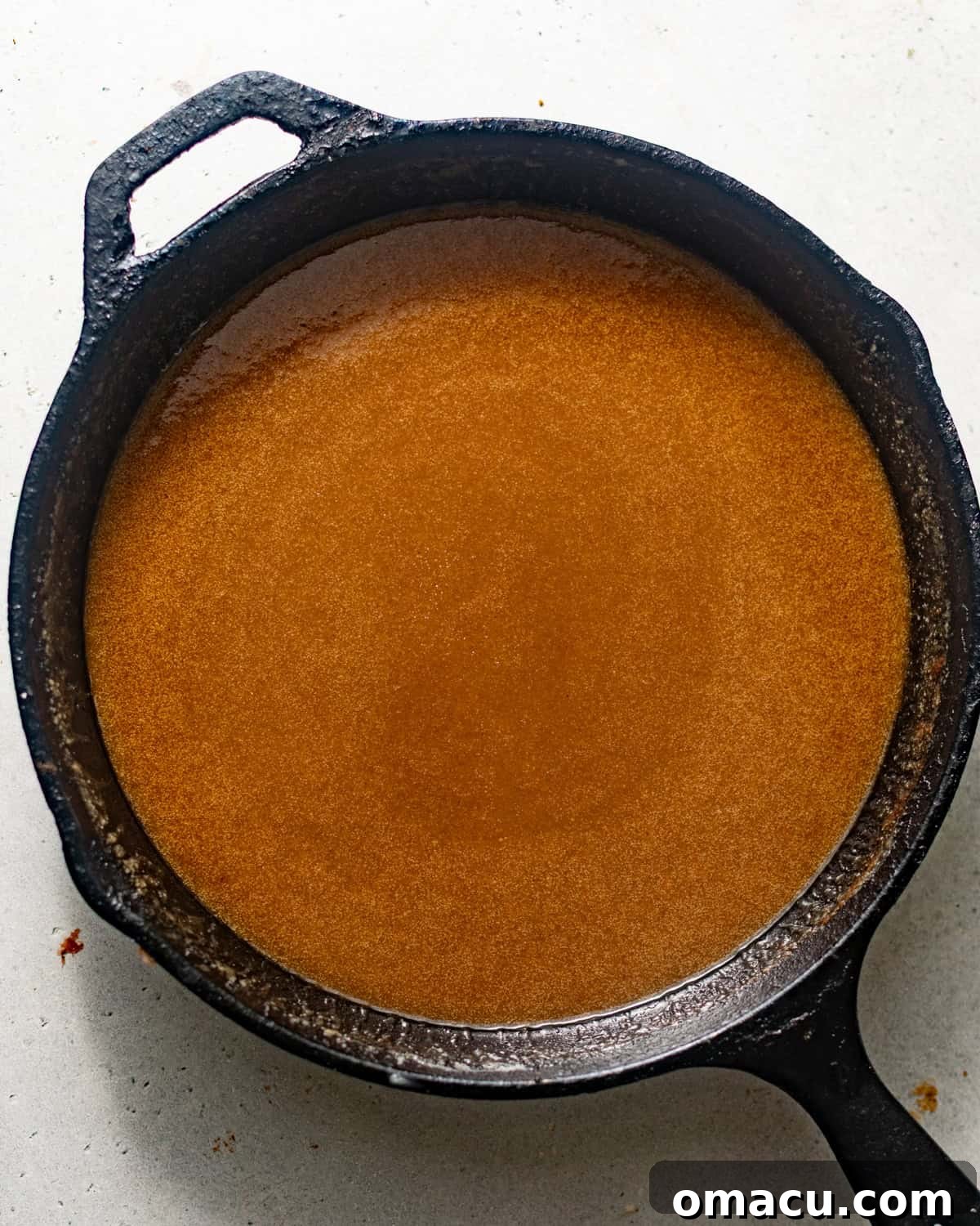 Rich caramel sauce bubbling gently in a skillet, forming the base of the pecan pie filling.